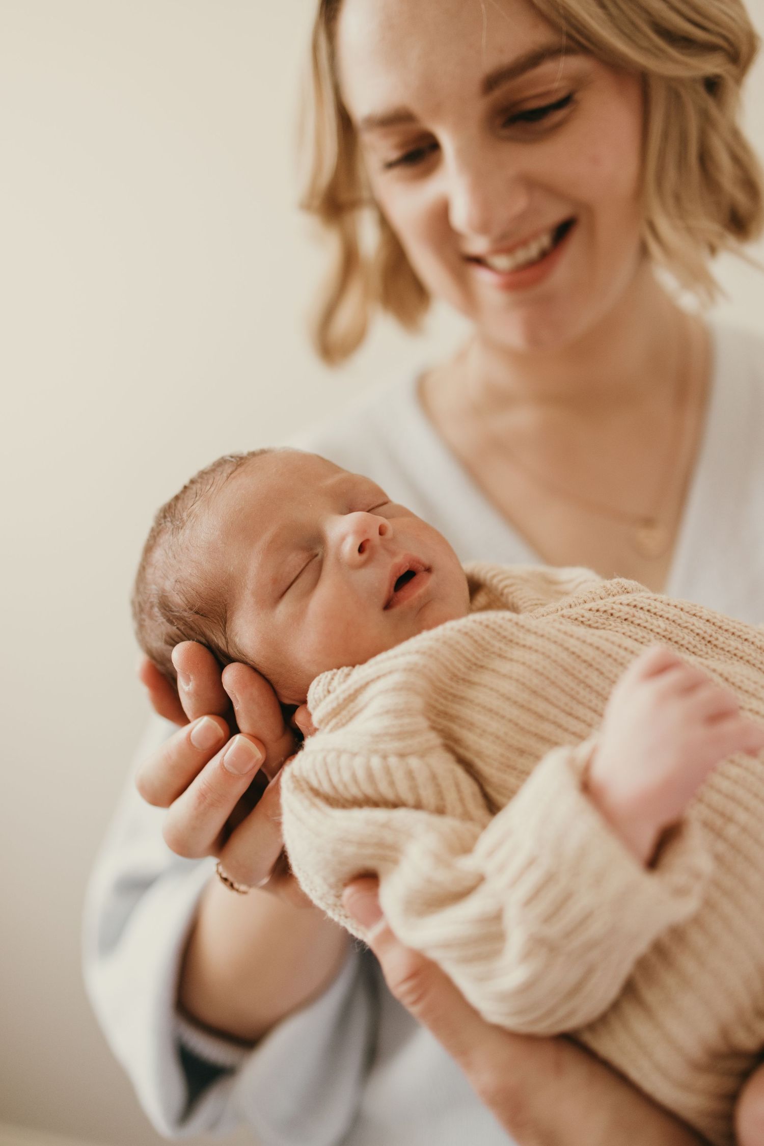 Gentle moment between parent and sleeping newborn wearing a soft beige sweater.