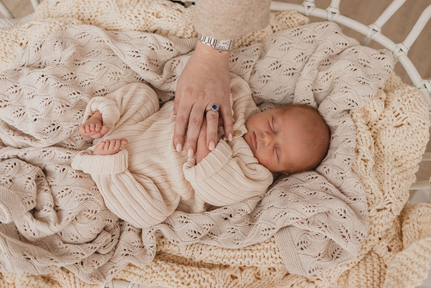Newborn baby sleeping peacefully on a cream knit blanket with a gentle hand resting nearby.