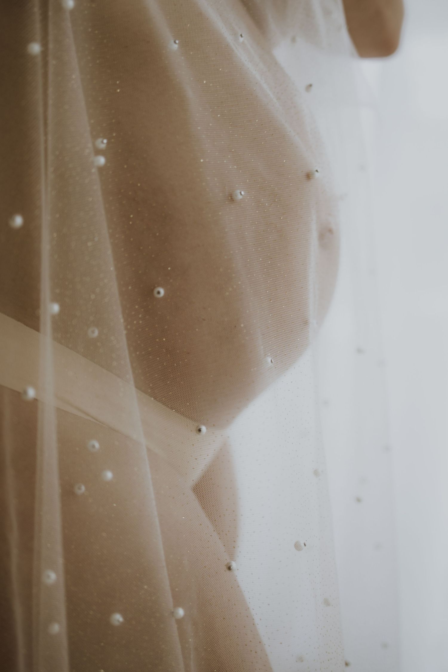 Close-up of a bridal veil with pearl embellishments draped over a nude wedding dress.
