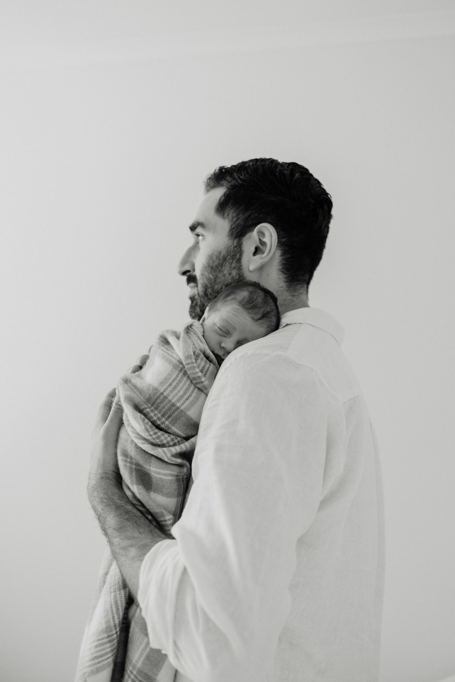 Black and white portrait of a parent cradling an infant wrapped in a soft blanket.