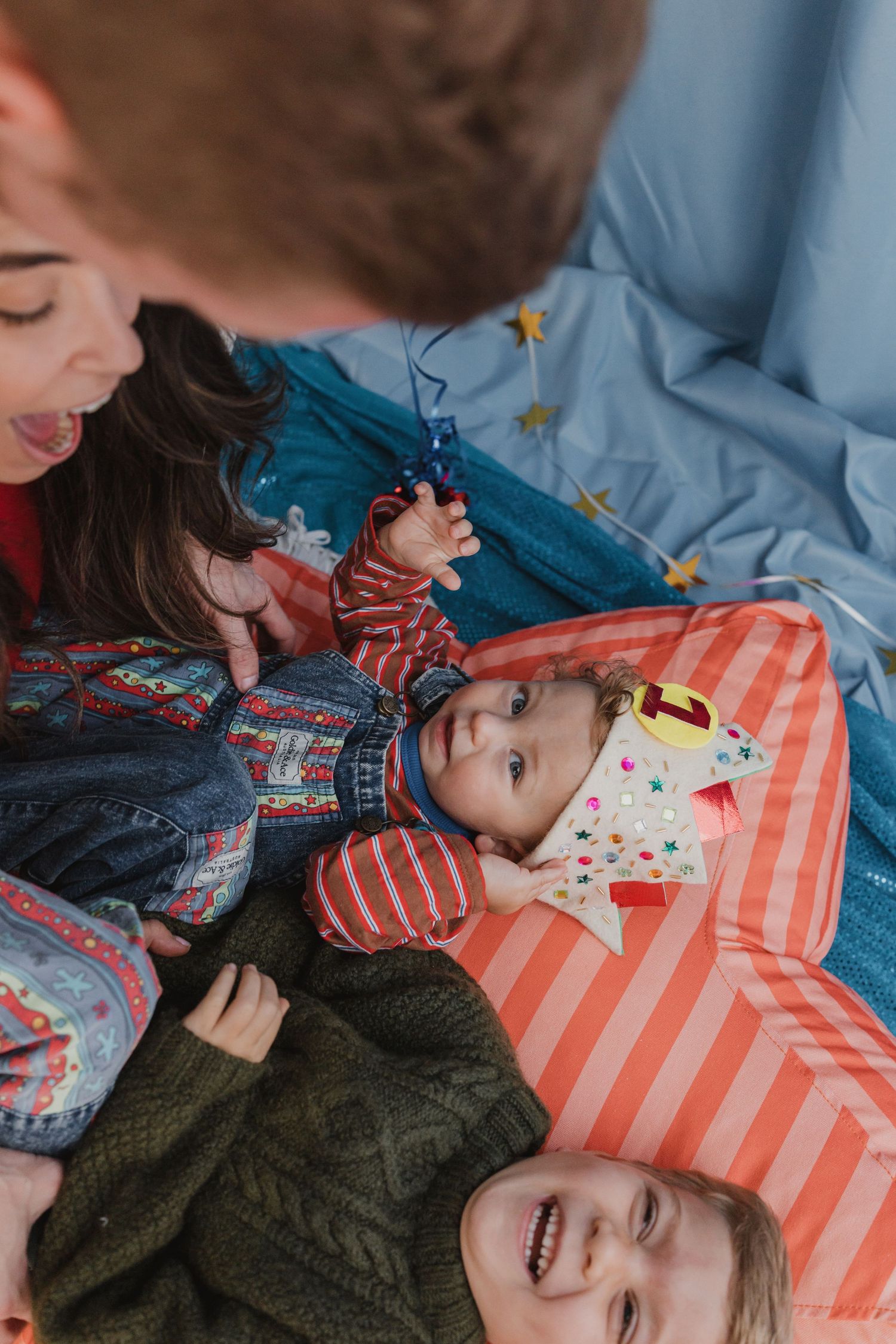 Family with newborn baby and two children lying on colorful bedding, sharing a joyful moment together.