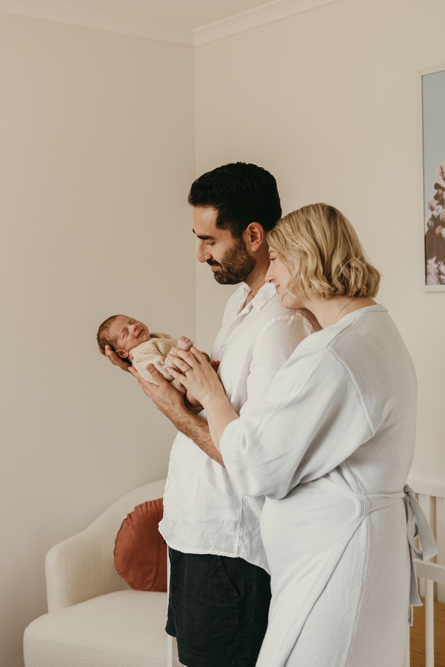 Intimate family moment captured in a nursery with parents lovingly gazing at their newborn.