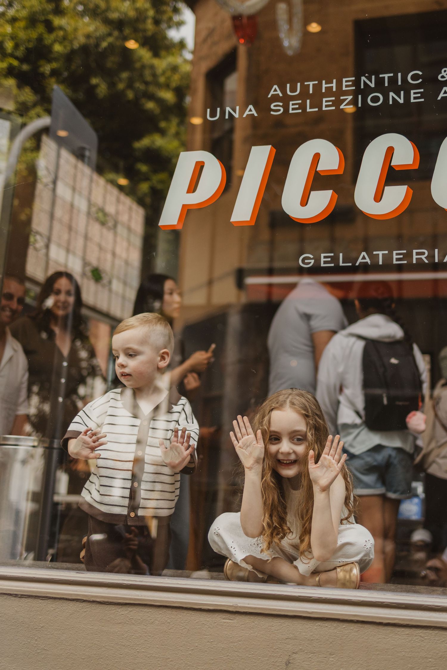 Two children press their faces against the window of Piccolo Gelateria ice cream shop.