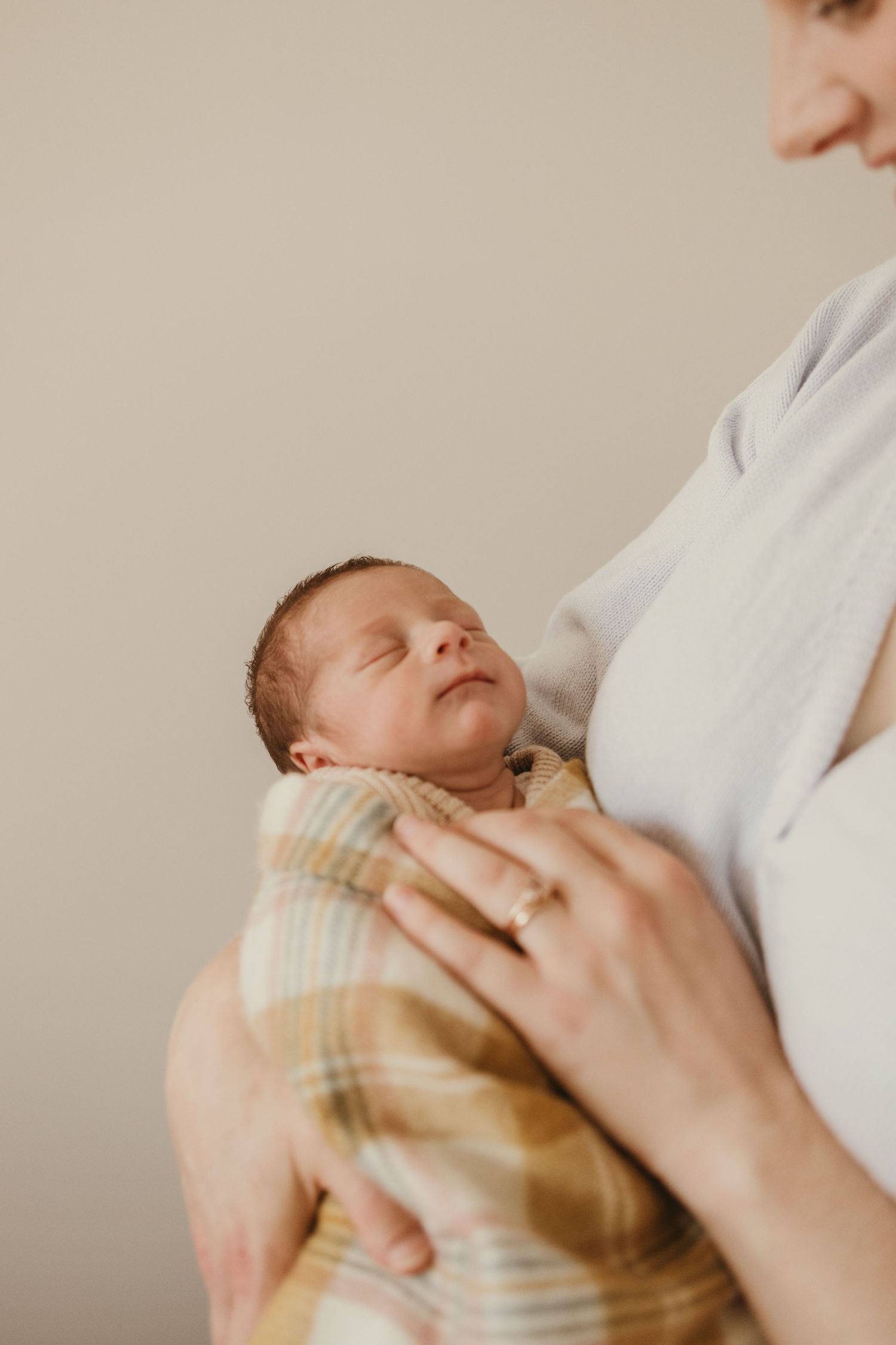 Close up of sleeping newborn wrapped in plaid blanket being held against white clothing.