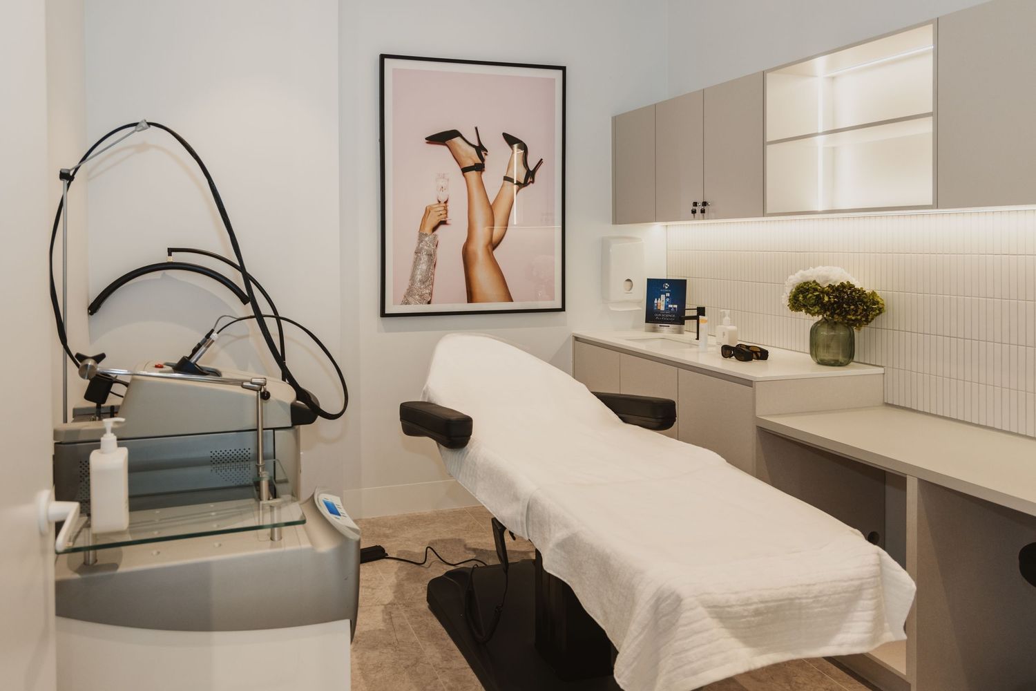 Modern medical spa treatment room with massage table, laser equipment, and elegant decor featuring a fashion art print.