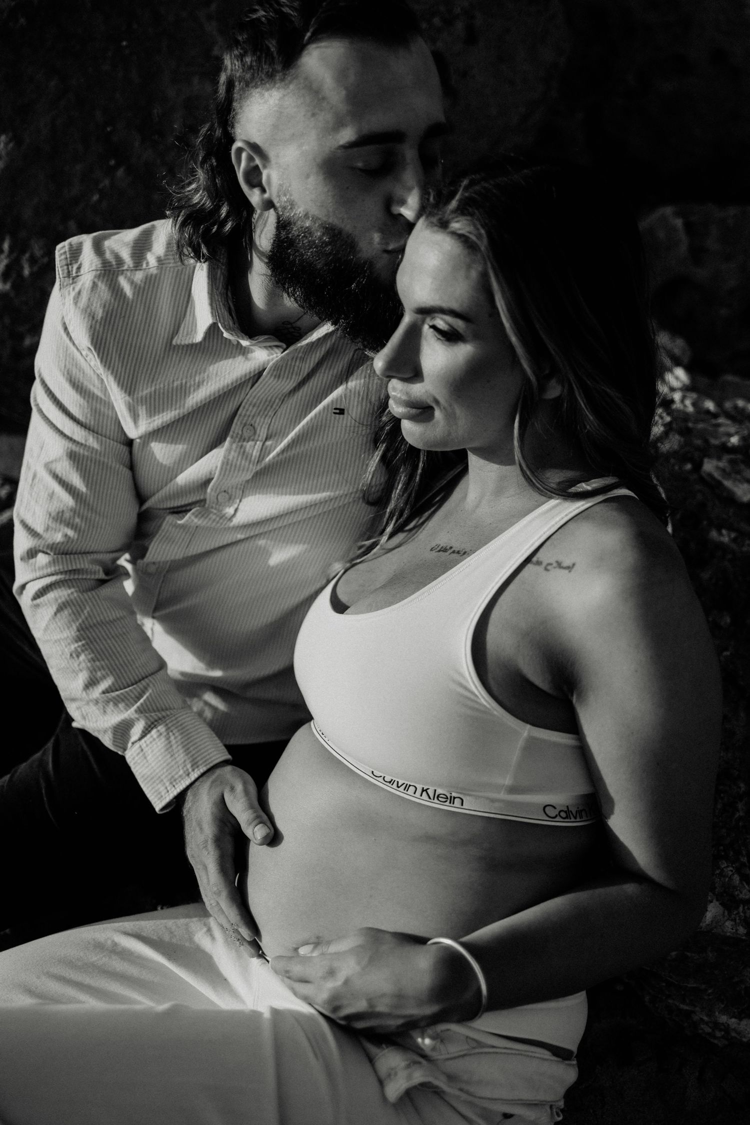 Black and white maternity photo of couple, bearded man kissing pregnant woman wearing Calvin Klein underwear.