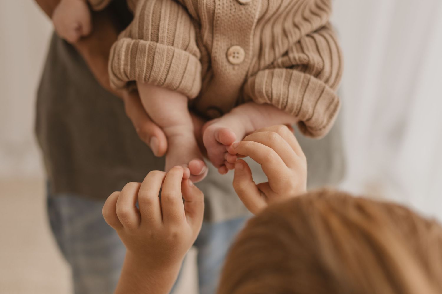 Two young children holding hands together, wearing cozy knit sweaters in warm neutral tones.