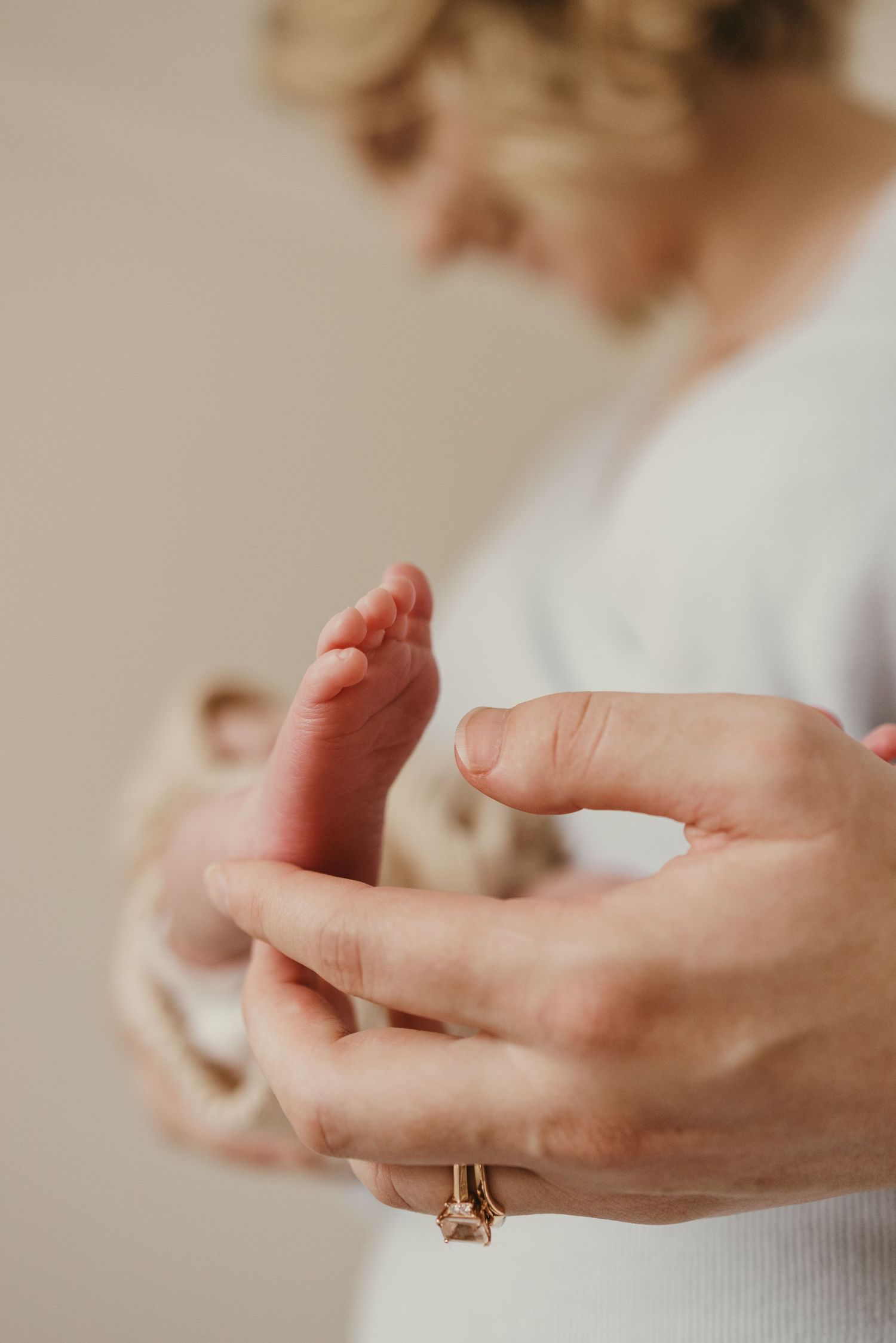 Close-up of tiny newborn baby foot being held by gentle hands with wedding ring.