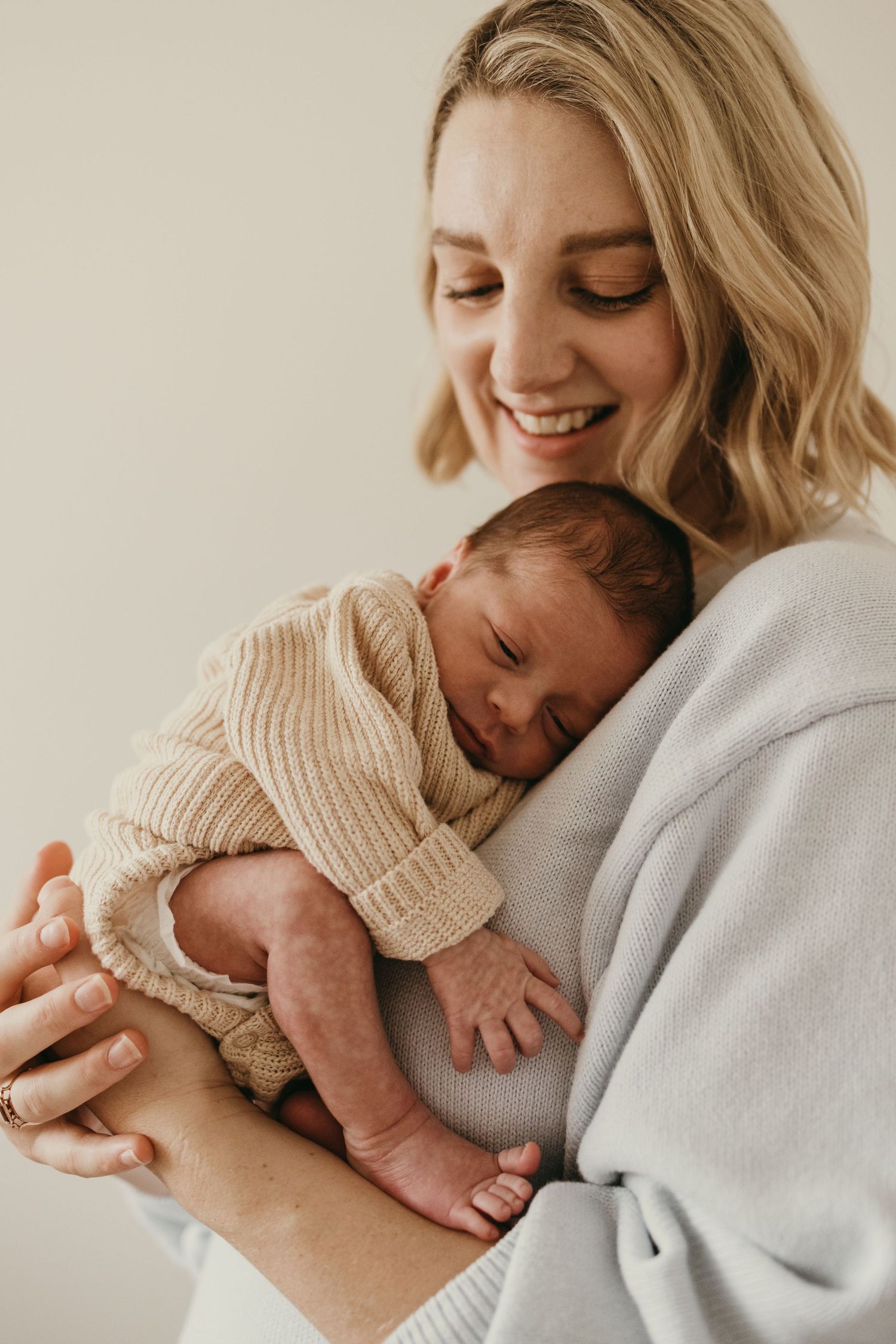 Candid moment of parent holding sleeping newborn wearing knit sweater against neutral background.