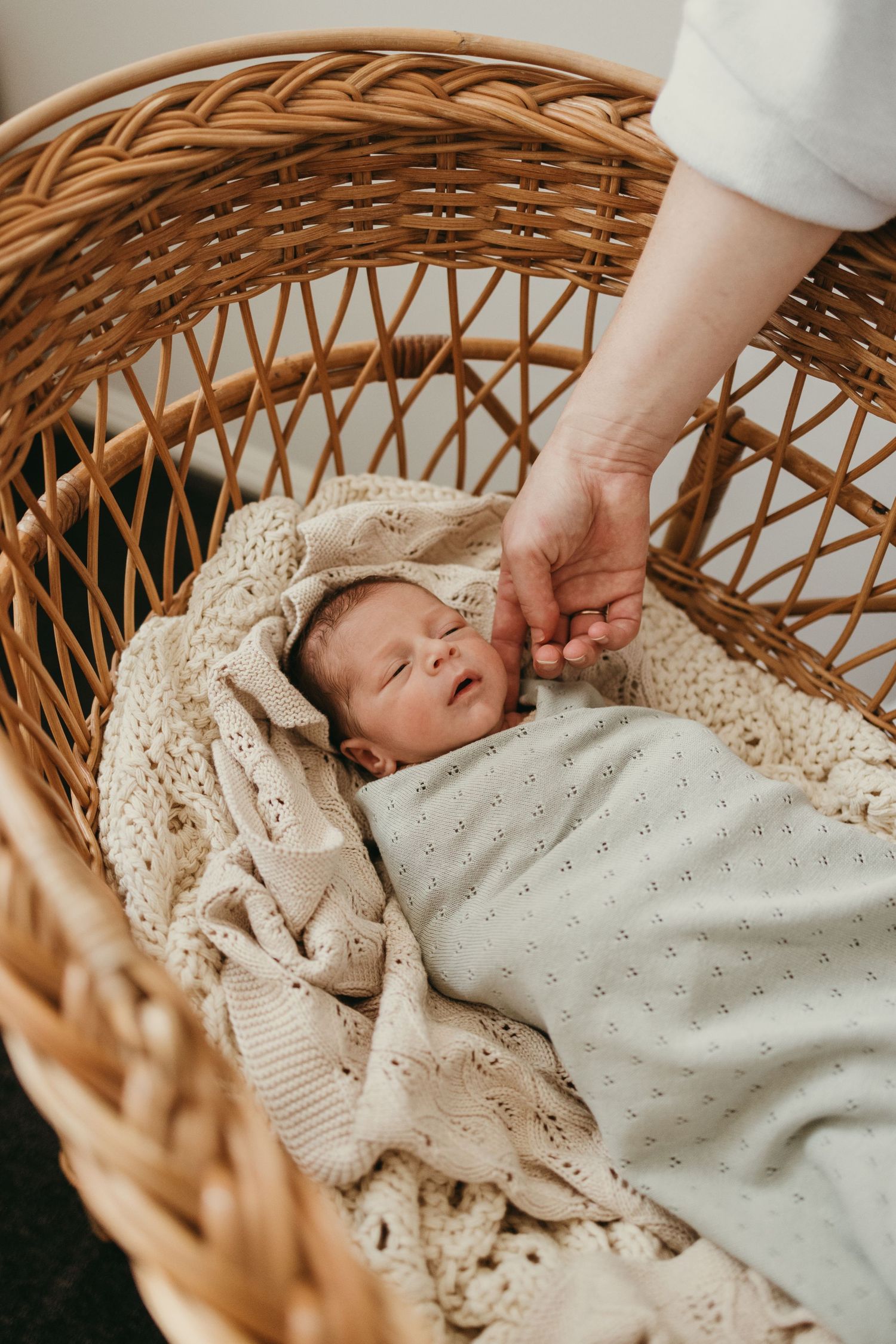 Black and white portrait of a sleeping newborn baby tucked into cozy blankets in a wicker bassinet.