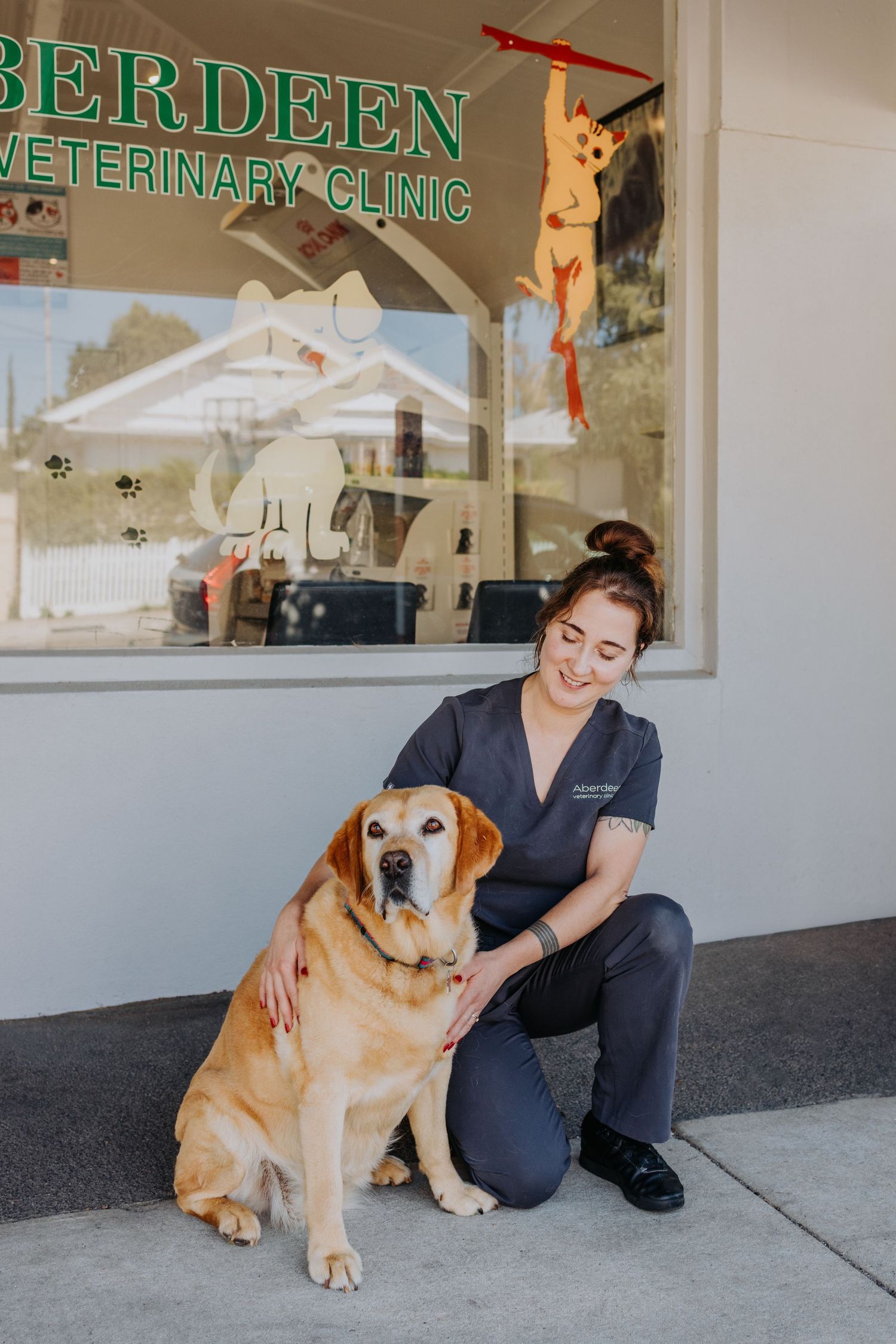 Veterinary staff member in scrubs kneeling beside a golden Labrador outside Aberdeen Veterinary Clinic.