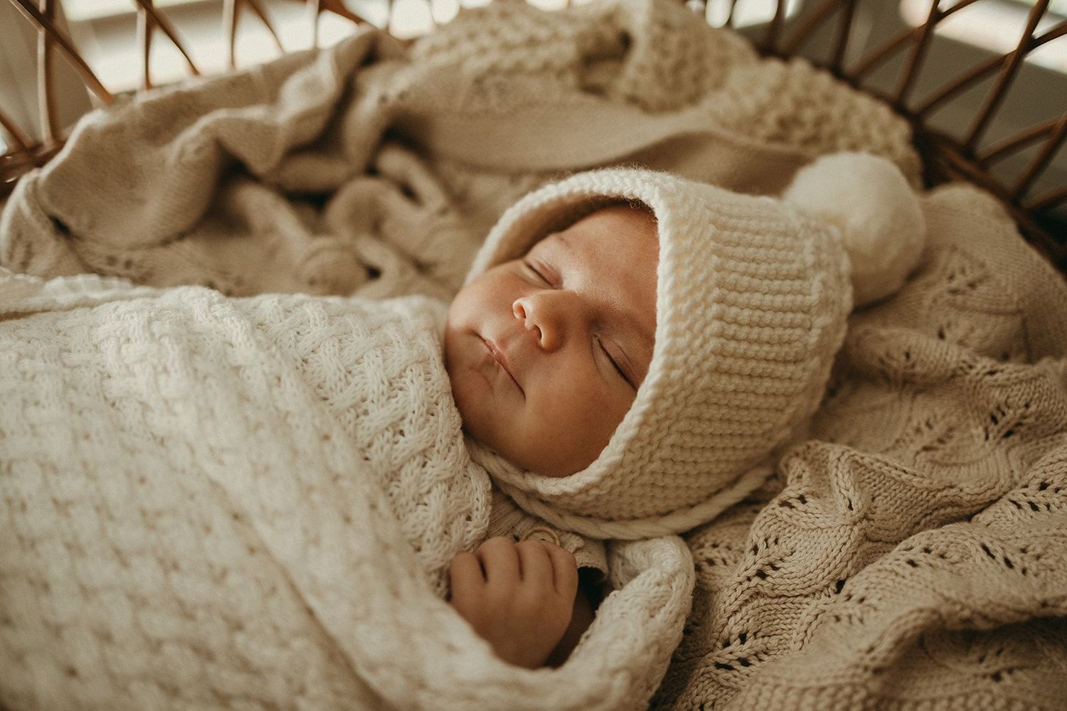 Geelong newborn photography - sleeping newborn baby wrapped in a cream knit blanket and bonnet in a wicker bassinet.