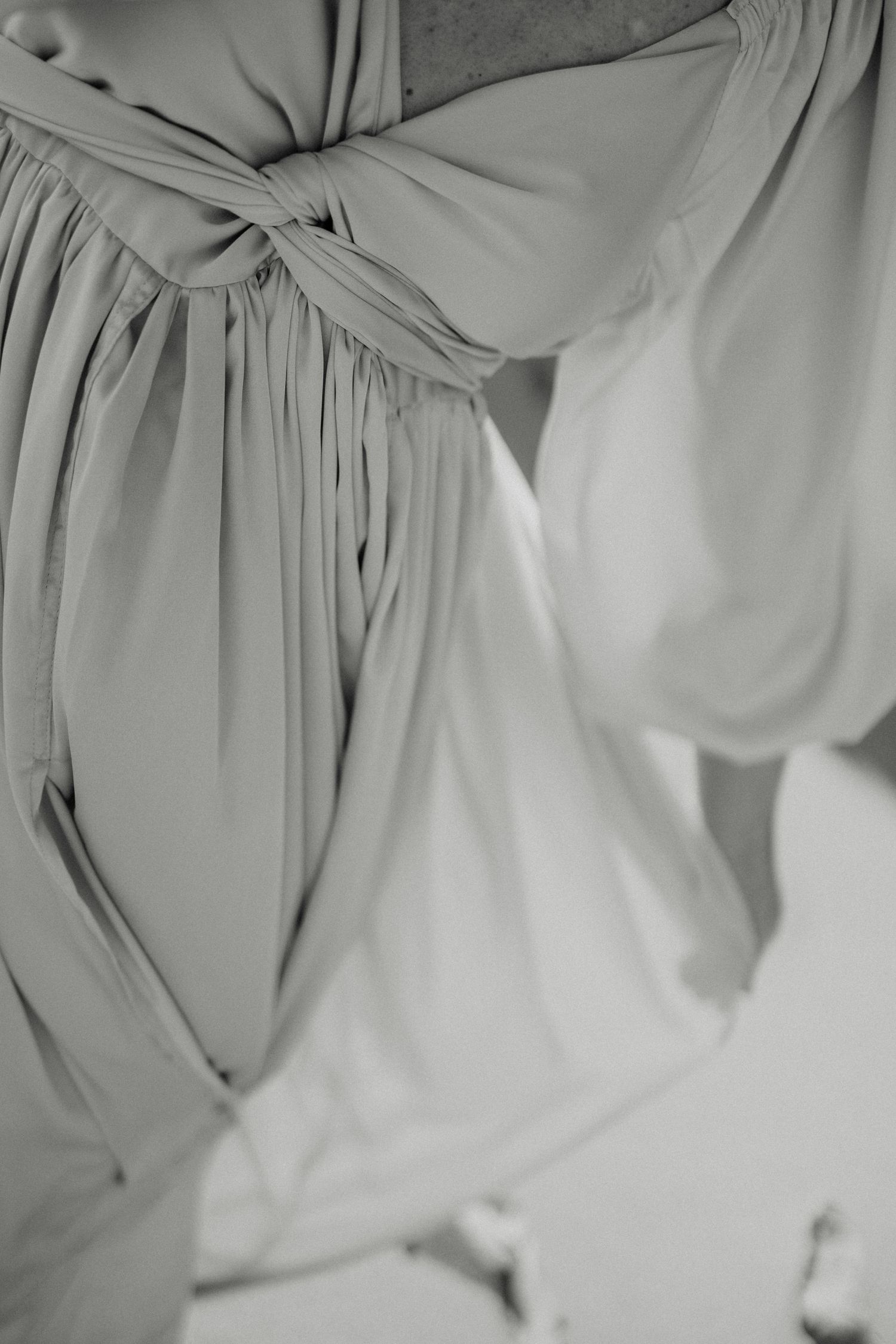 Black and white close-up of elegant draped fabric with a knotted waist detail on a flowing gown.