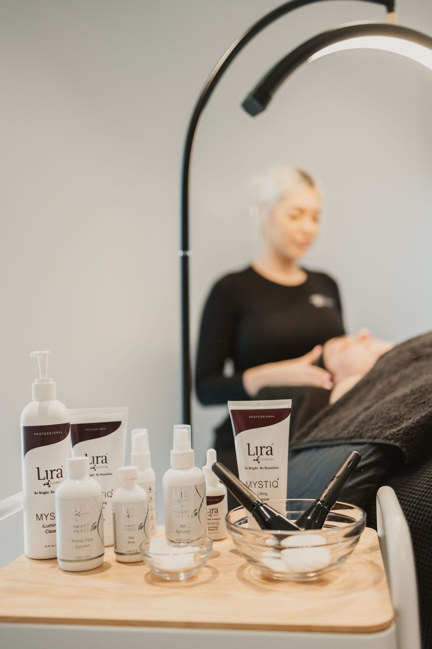Lira skincare products displayed on a salon cart while an esthetician performs a facial treatment on a client.