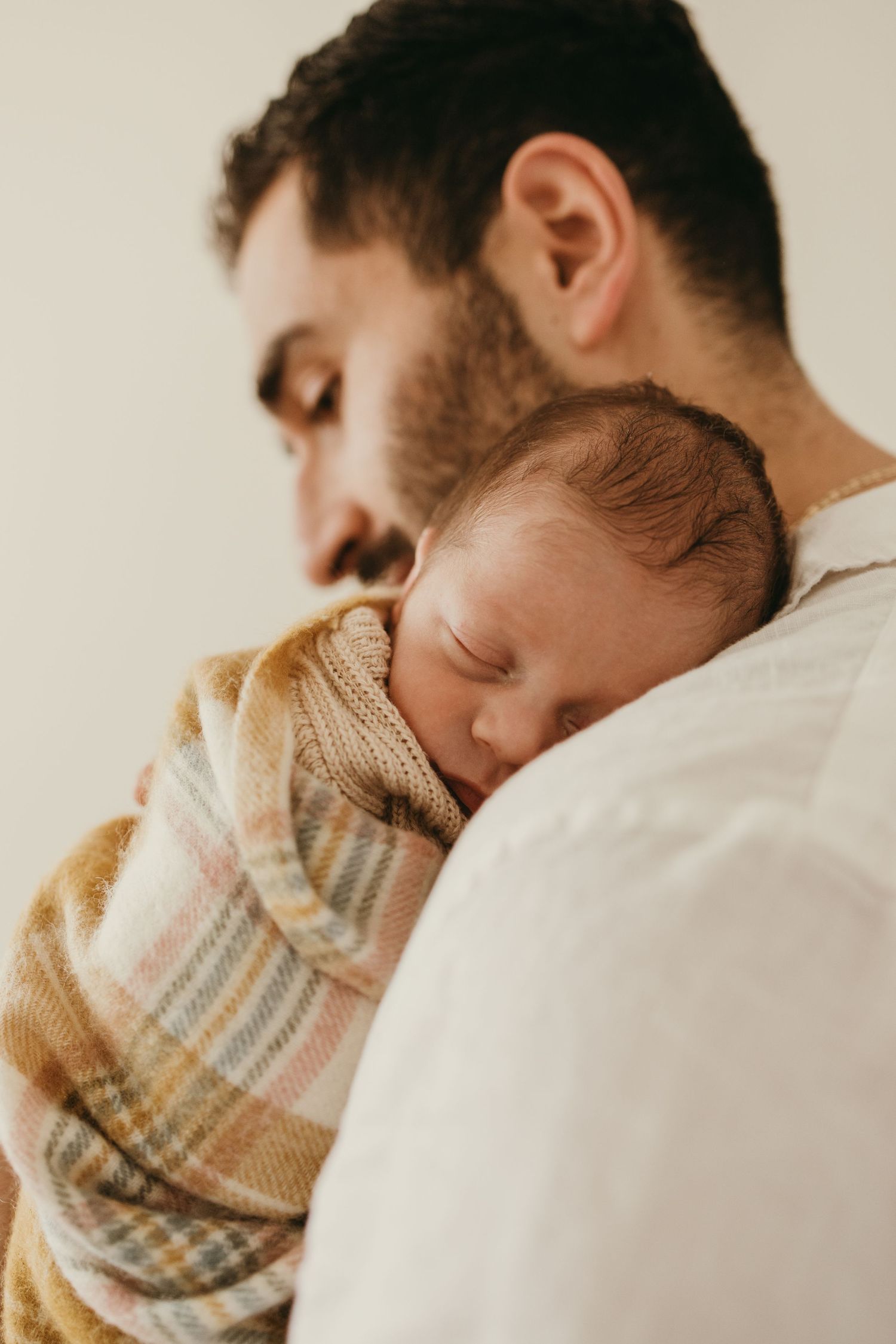Intimate moment showing a parent and sleeping baby wrapped in a warm plaid blanket.