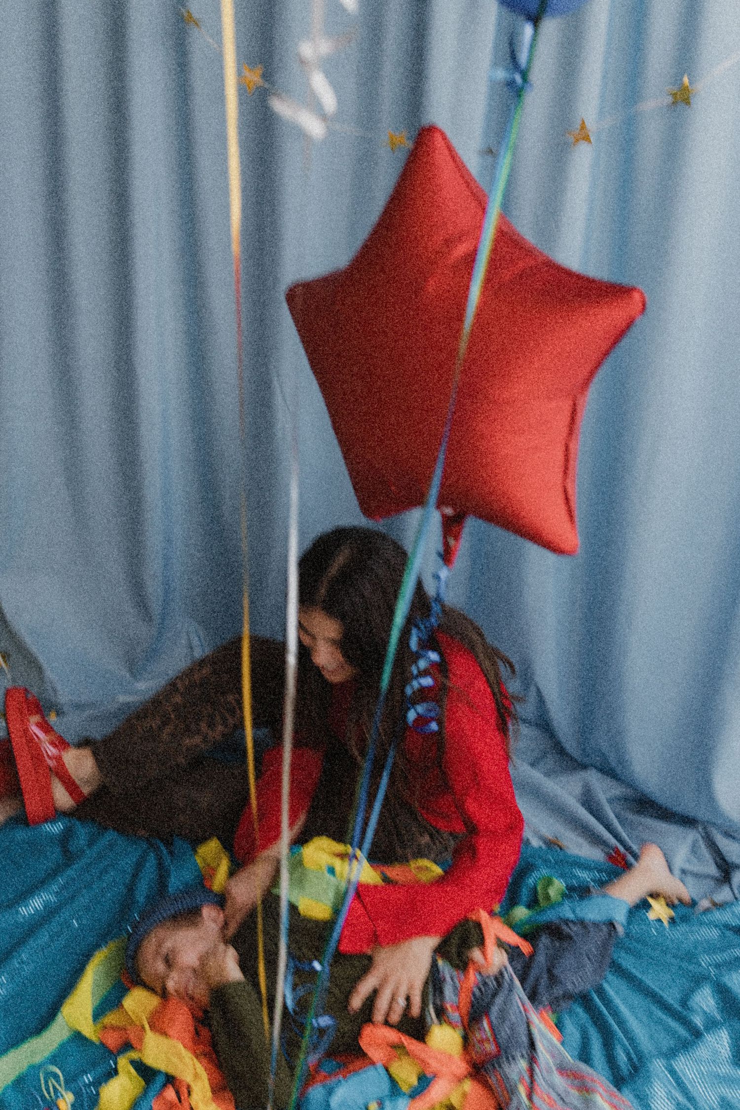 Woman in red dress sitting on colorful confetti floor with a red star balloon at a festive celebration.