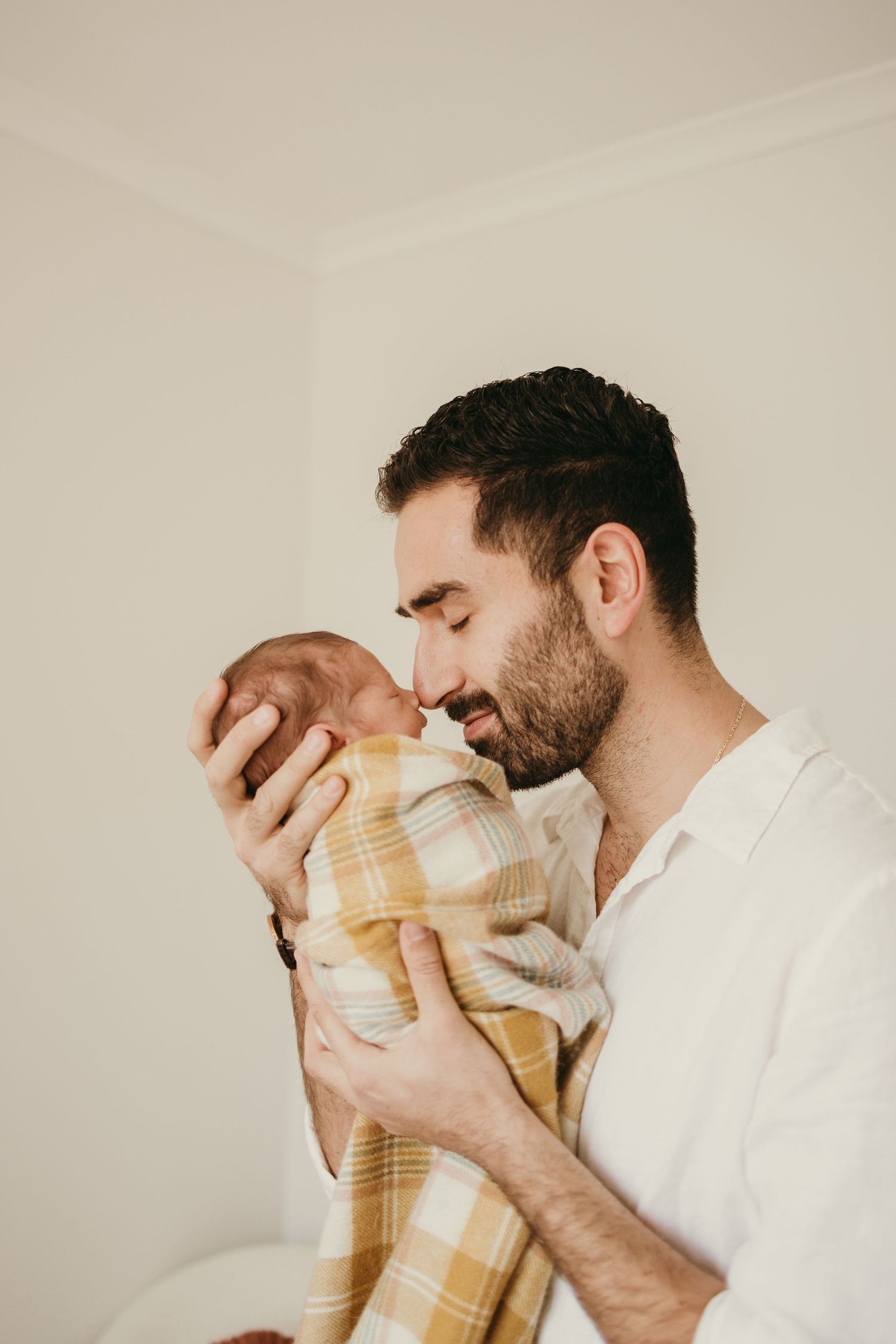 Close-up of a gentle moment between parent and newborn swaddled in plaid.