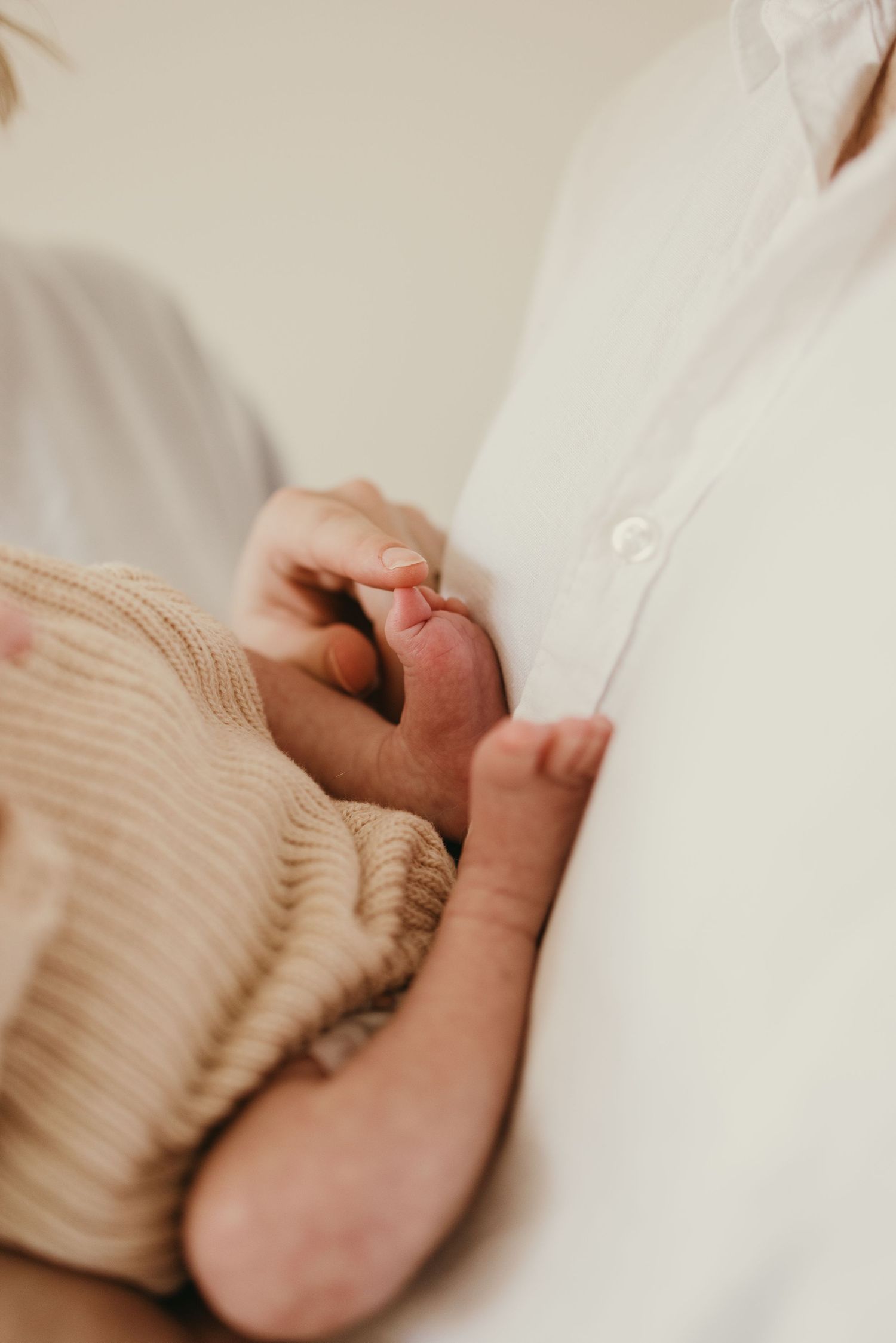Close-up shot of tiny newborn feet being gently held against white clothing.