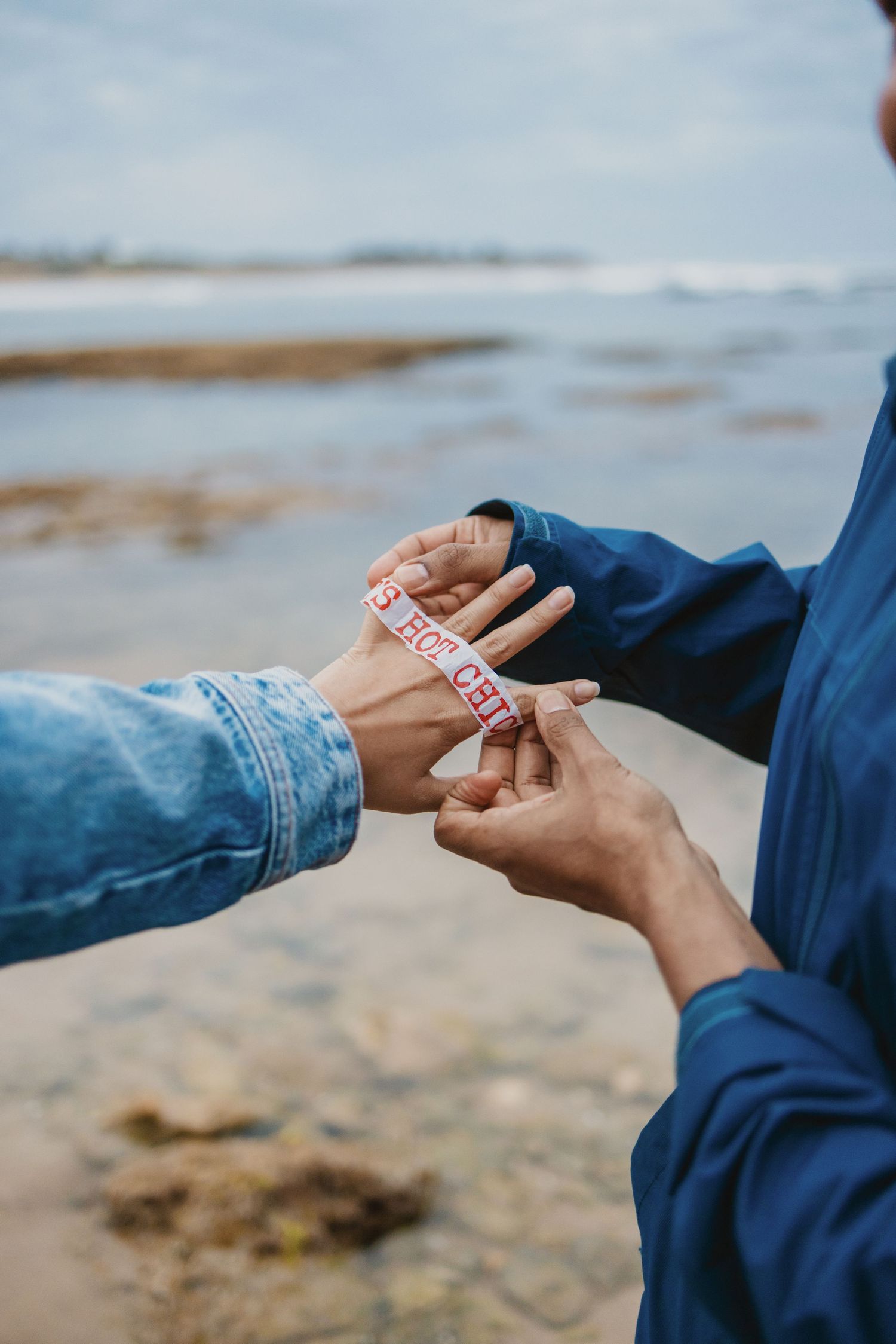 Close-up of couple exchanging a festival wristband on a rocky beach shoreline.