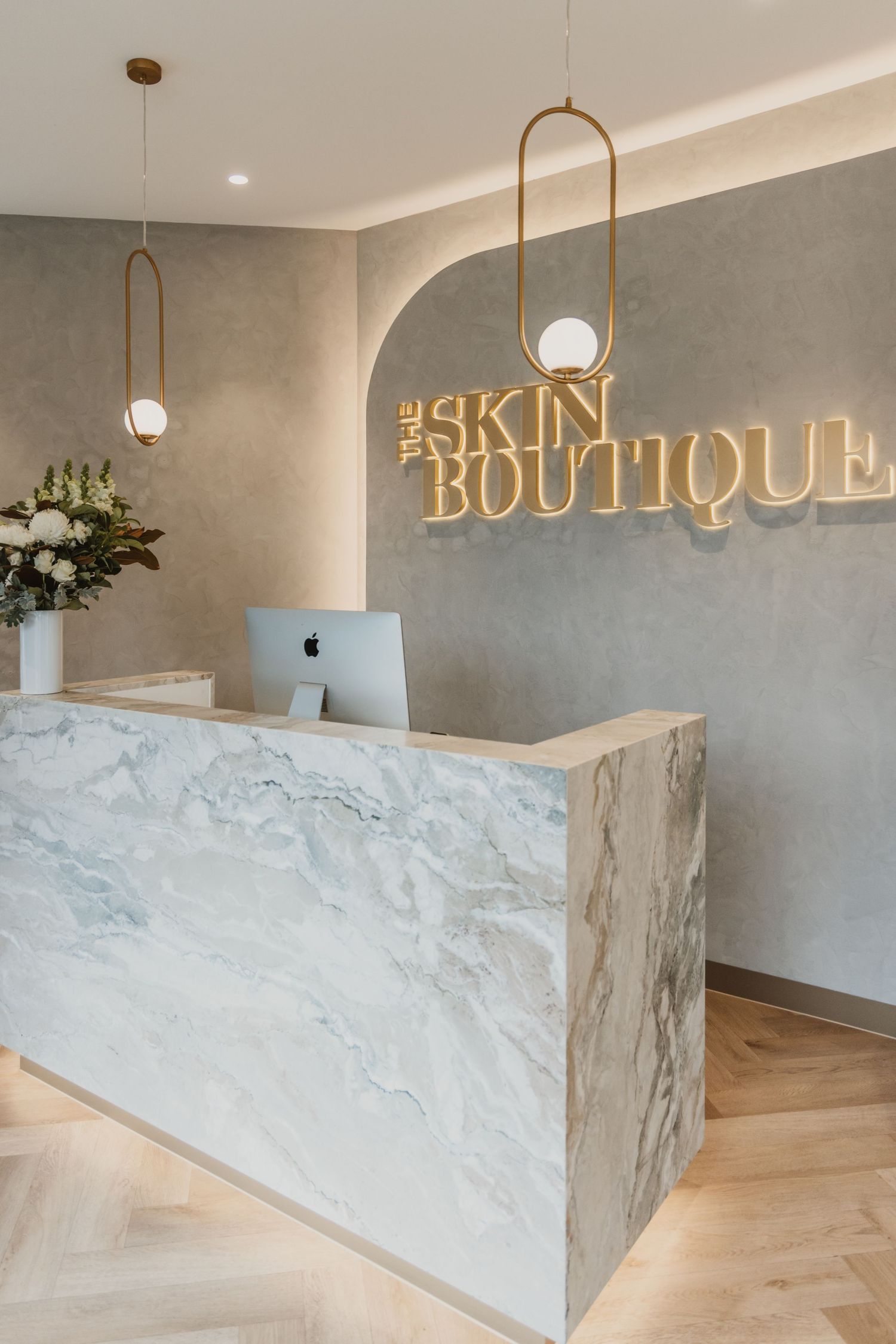 Elegant marble reception desk at The Skin Boutique with gold pendant lights and herringbone wood floors.