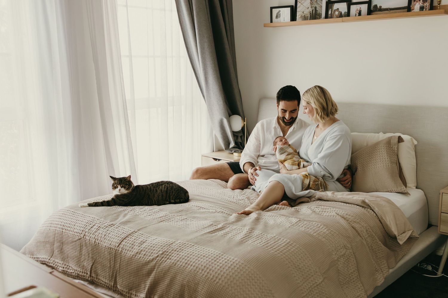 Cozy bedroom scene with couple in robes and black cat lounging on bed.