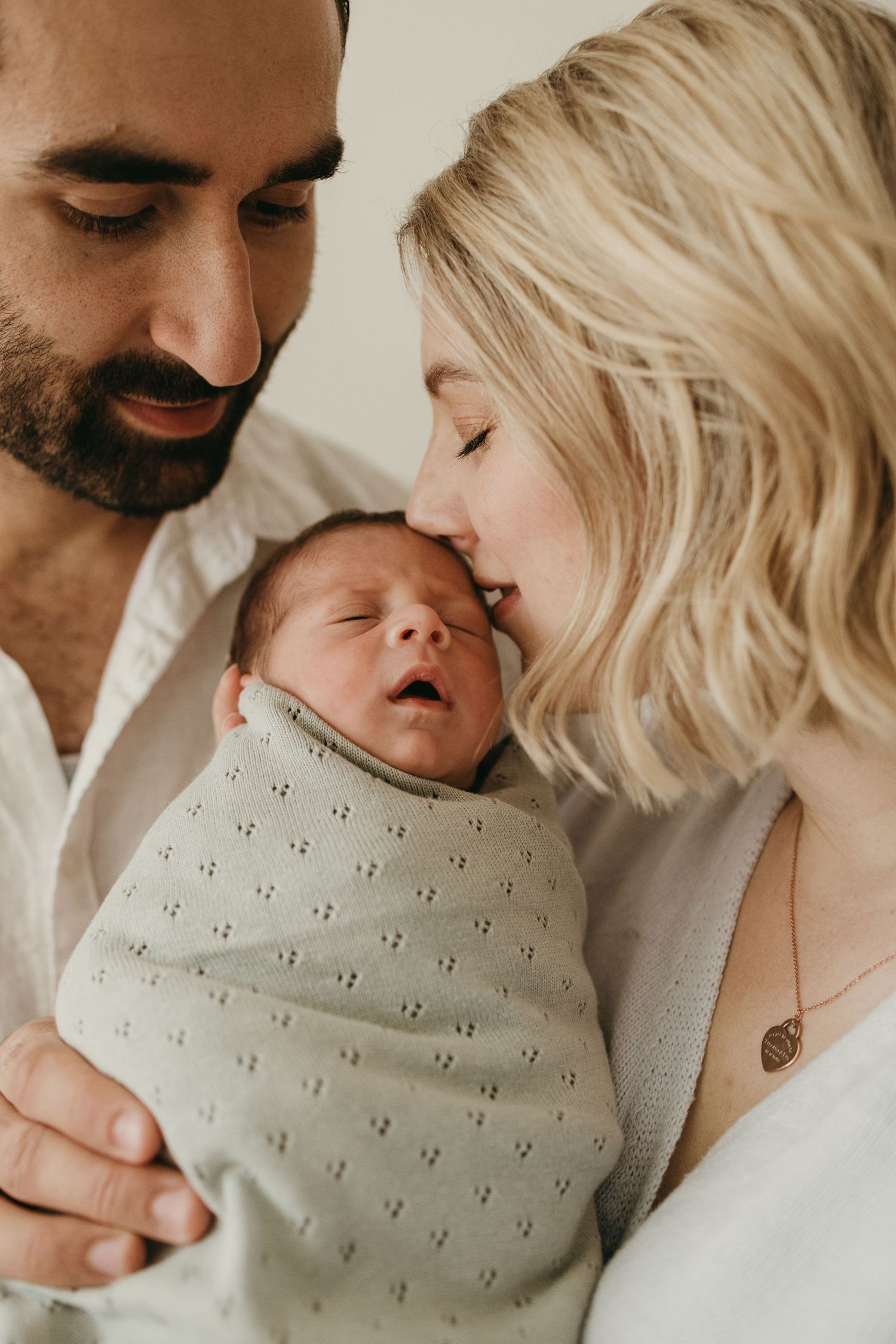 Close-up of parents sharing an intimate moment with their sleeping newborn wrapped in patterned blanket.