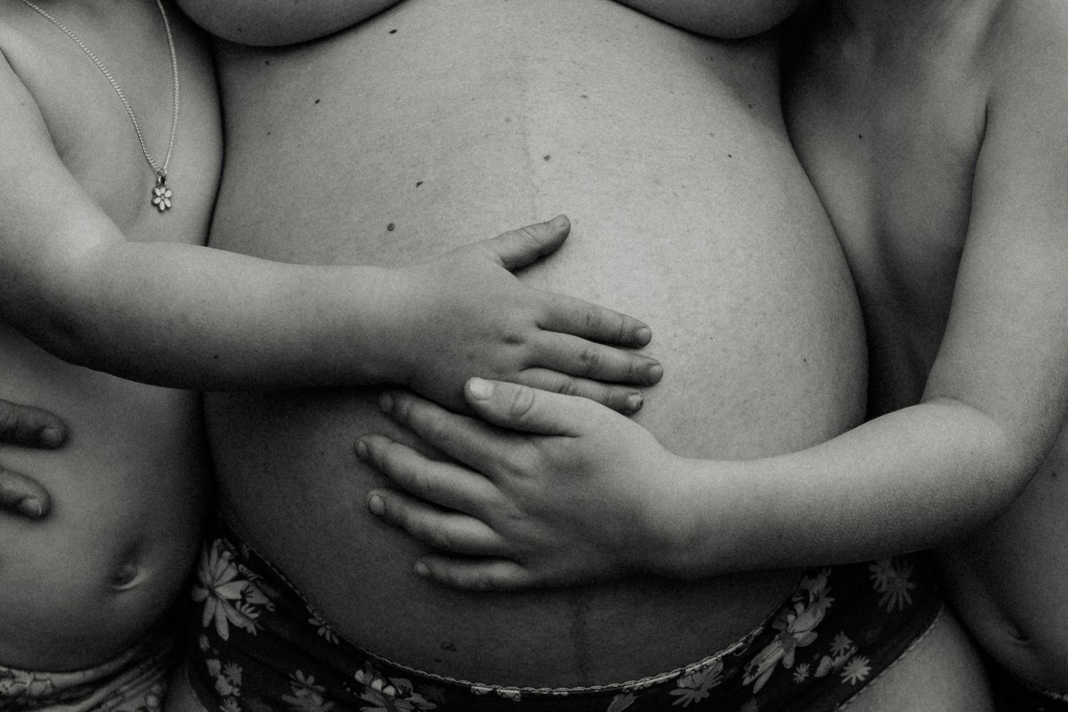 Black and white photo of a pregnant woman's belly with children's hands gently touching it.