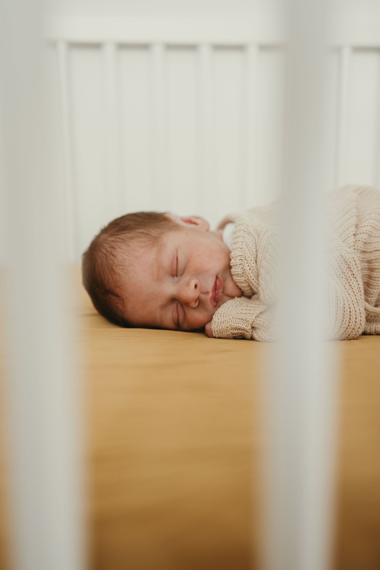 Sleeping baby viewed through crib slats in natural light.