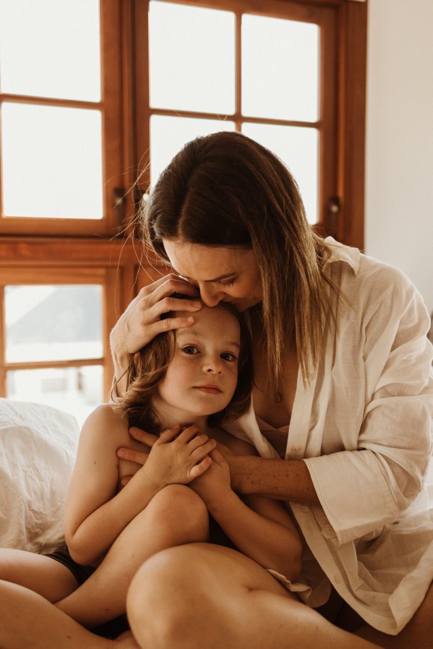 A tender moment shared between parent and child in white robes on a sunlit bed.