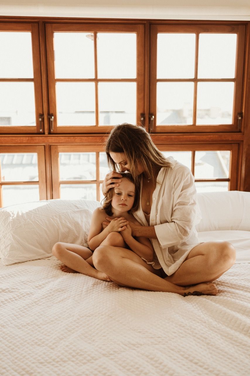 Peaceful morning scene with gentle embrace on white bedding by wooden windows.