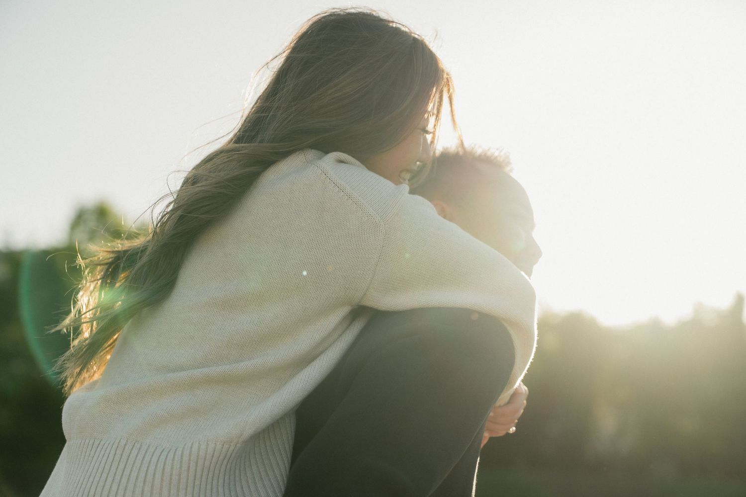 Two people sharing a warm embrace outdoors in golden backlit sunlight, conveying love and connection.