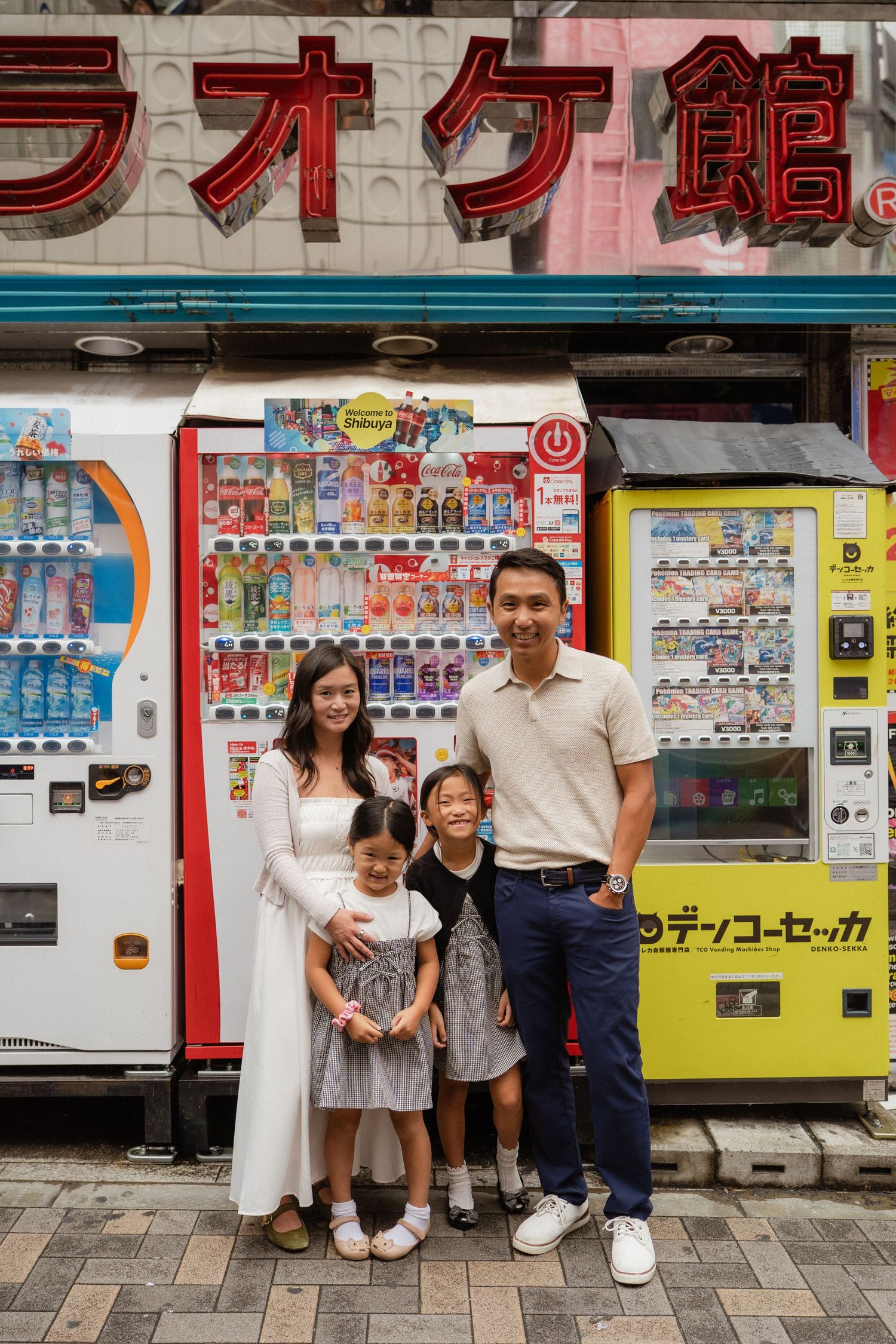 Family of four posing in front of Japanese vending machines and karaoke sign in Tokyo, Japan.