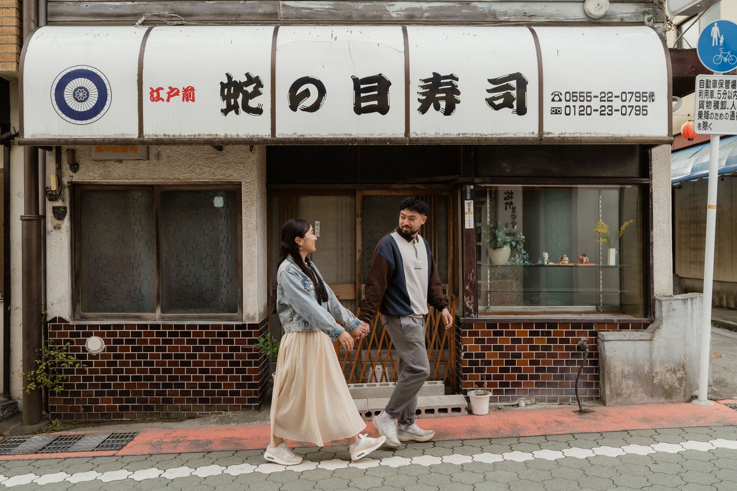 Couple walking in front of a traditional Japanese sushi restaurant with vintage signage in Japan.