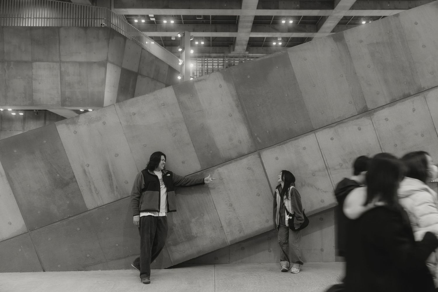 Black and white photo of people exploring a large concrete angular installation in a modern art gallery.