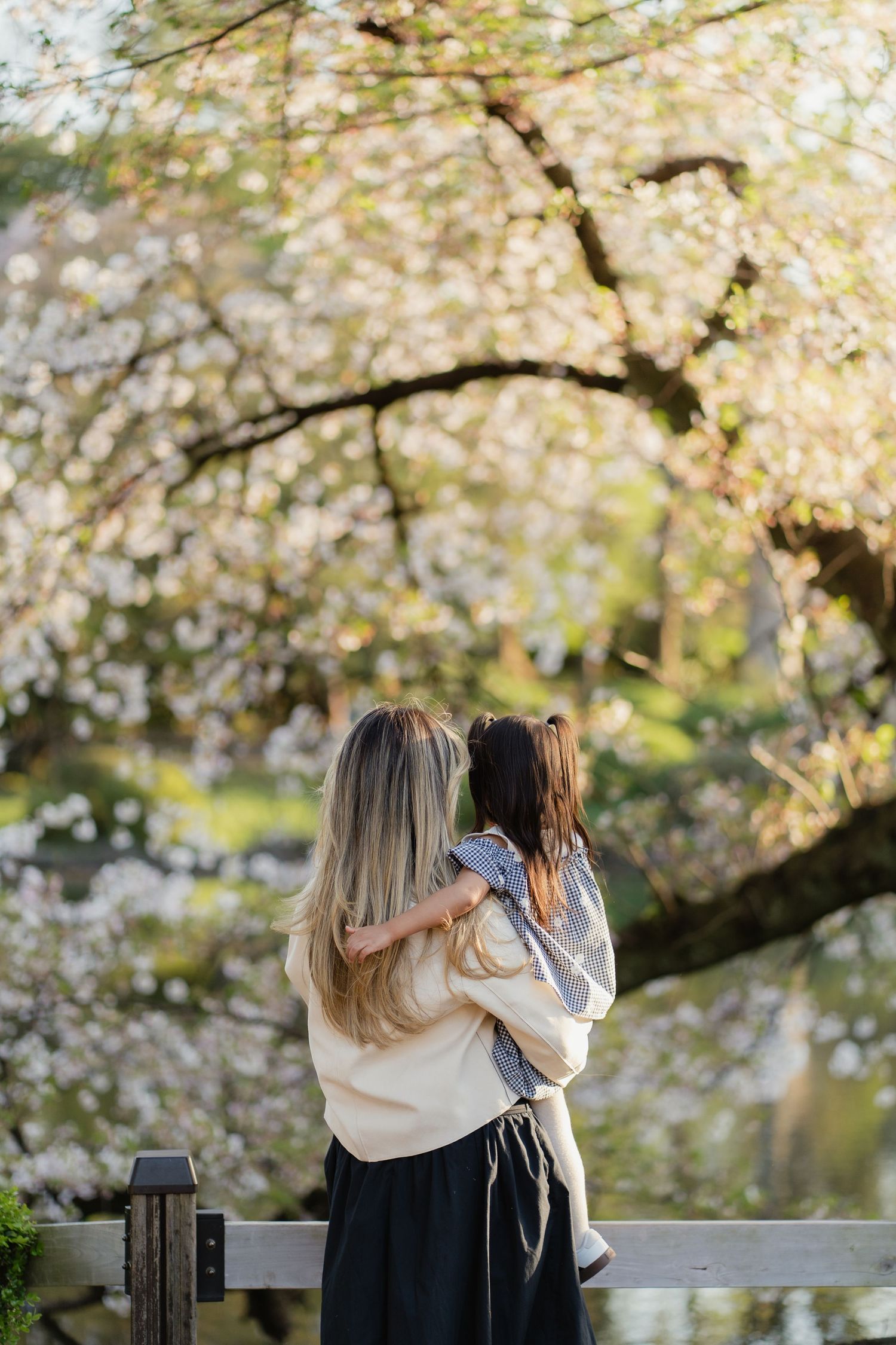 A mother holds her child while admiring cherry blossom trees in full bloom during spring.