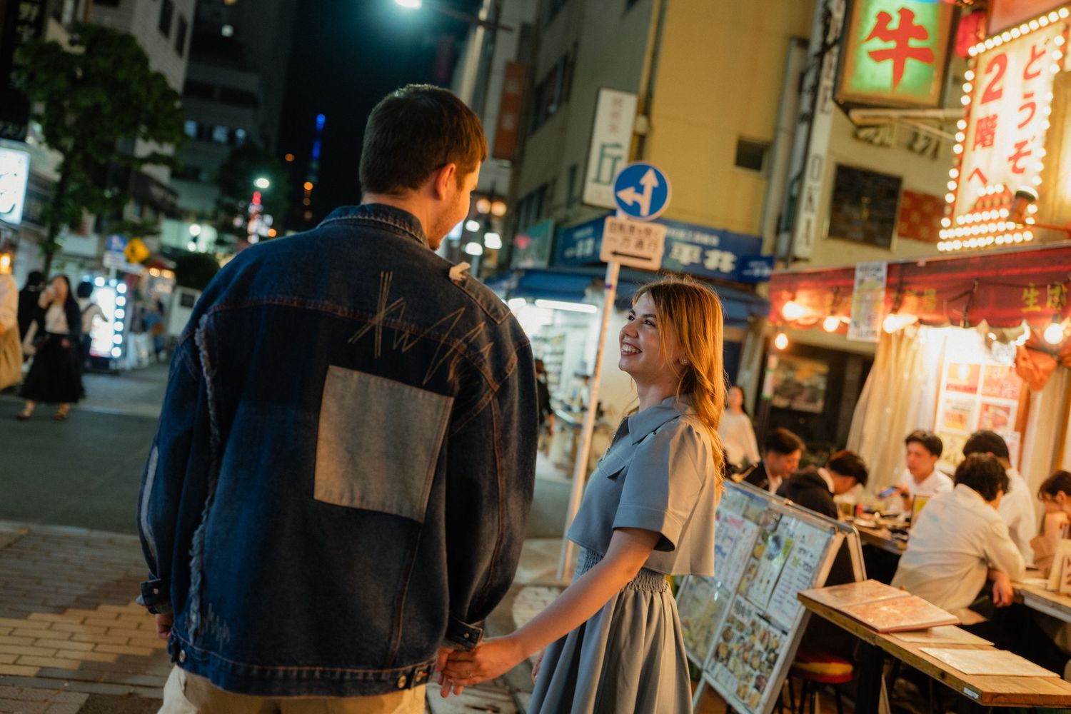 Couple holds hands while walking through a lively Tokyo street market at night.