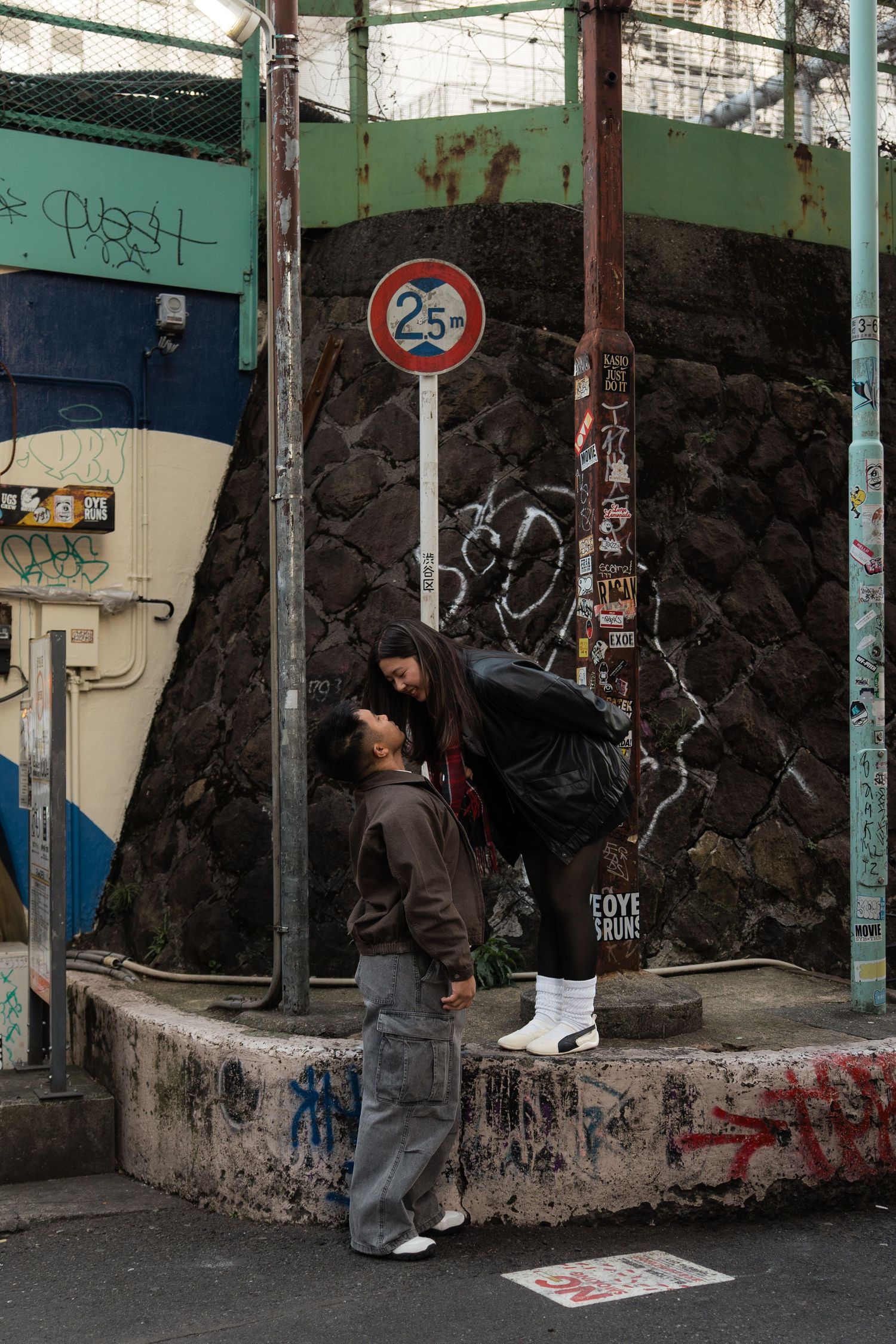 Two people share a tender moment on a graffiti-covered urban street corner near a 25 speed limit sign.