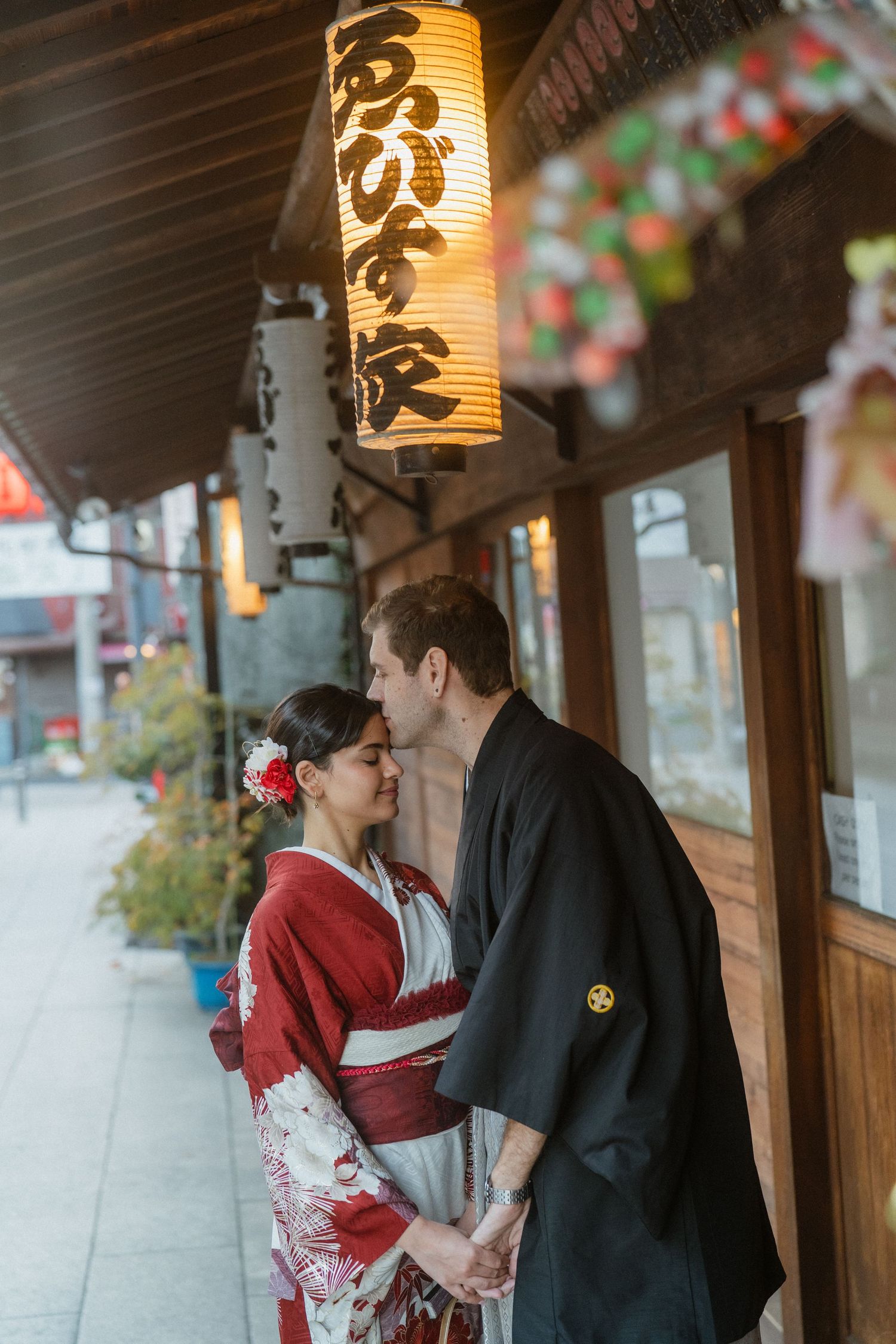 Couple in traditional Japanese kimono sharing a romantic moment under a glowing paper lantern on a Japanese street.