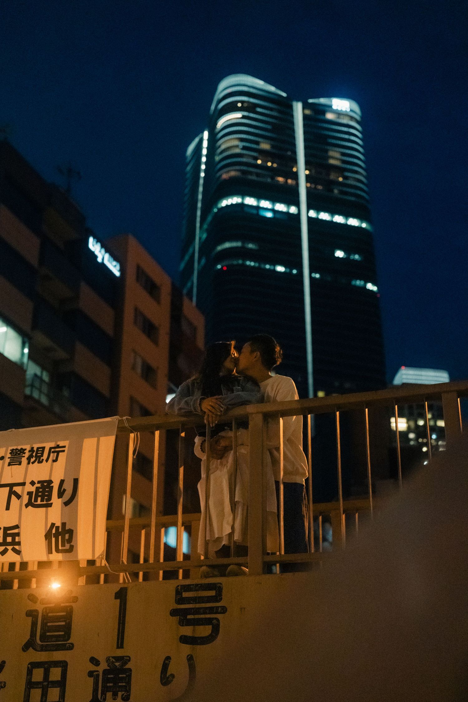 Couple standing on a bridge at night with illuminated skyscrapers in Tokyo, Japan.