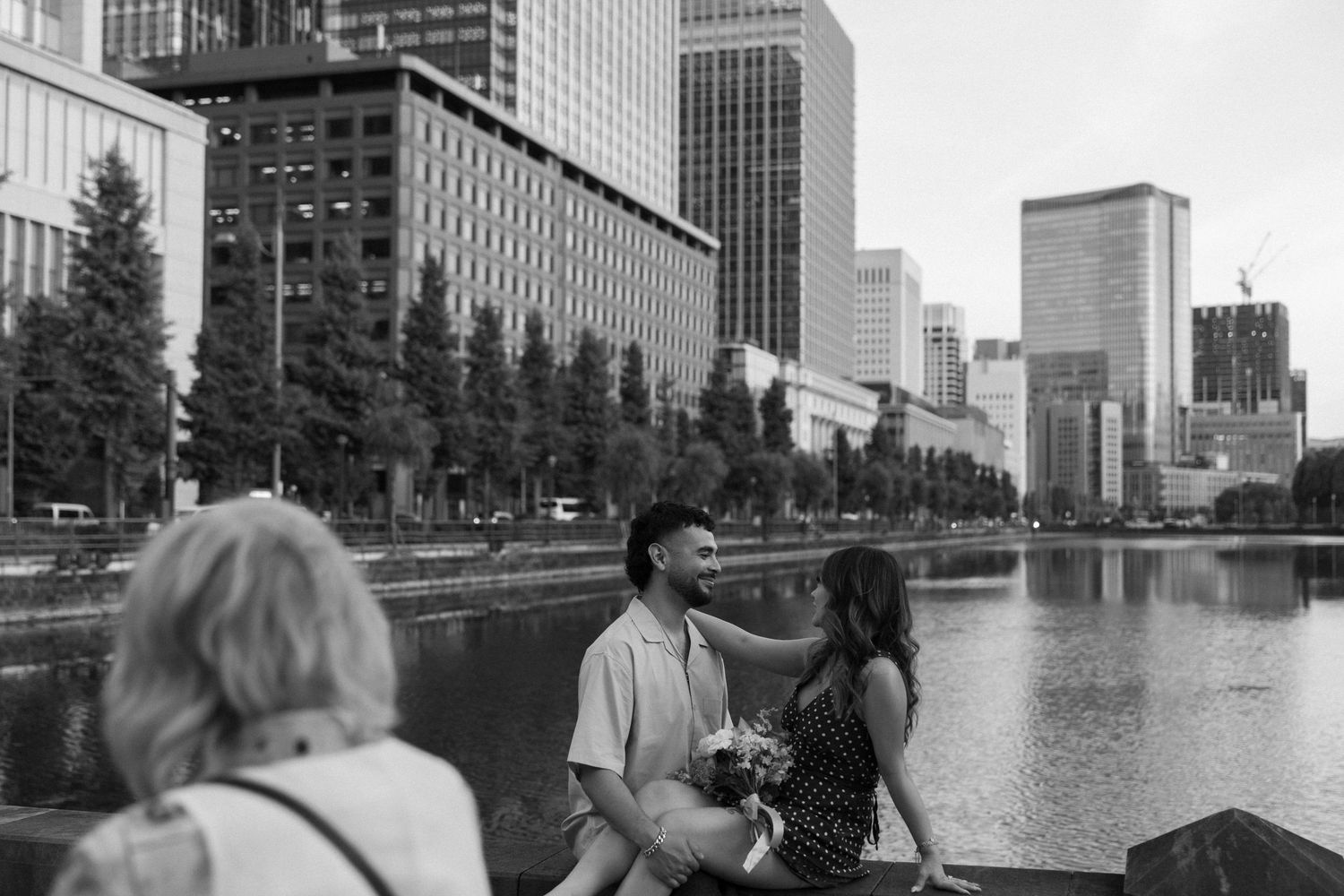 Couple sitting by a urban waterway with modern city skyscrapers reflecting in the background.