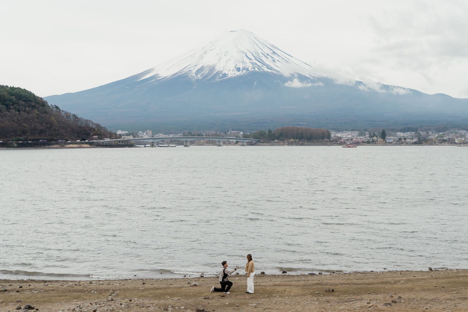 Couple on sandy shore of Lake Kawaguchi with iconic snow-capped Mount Fuji in background, Japan.