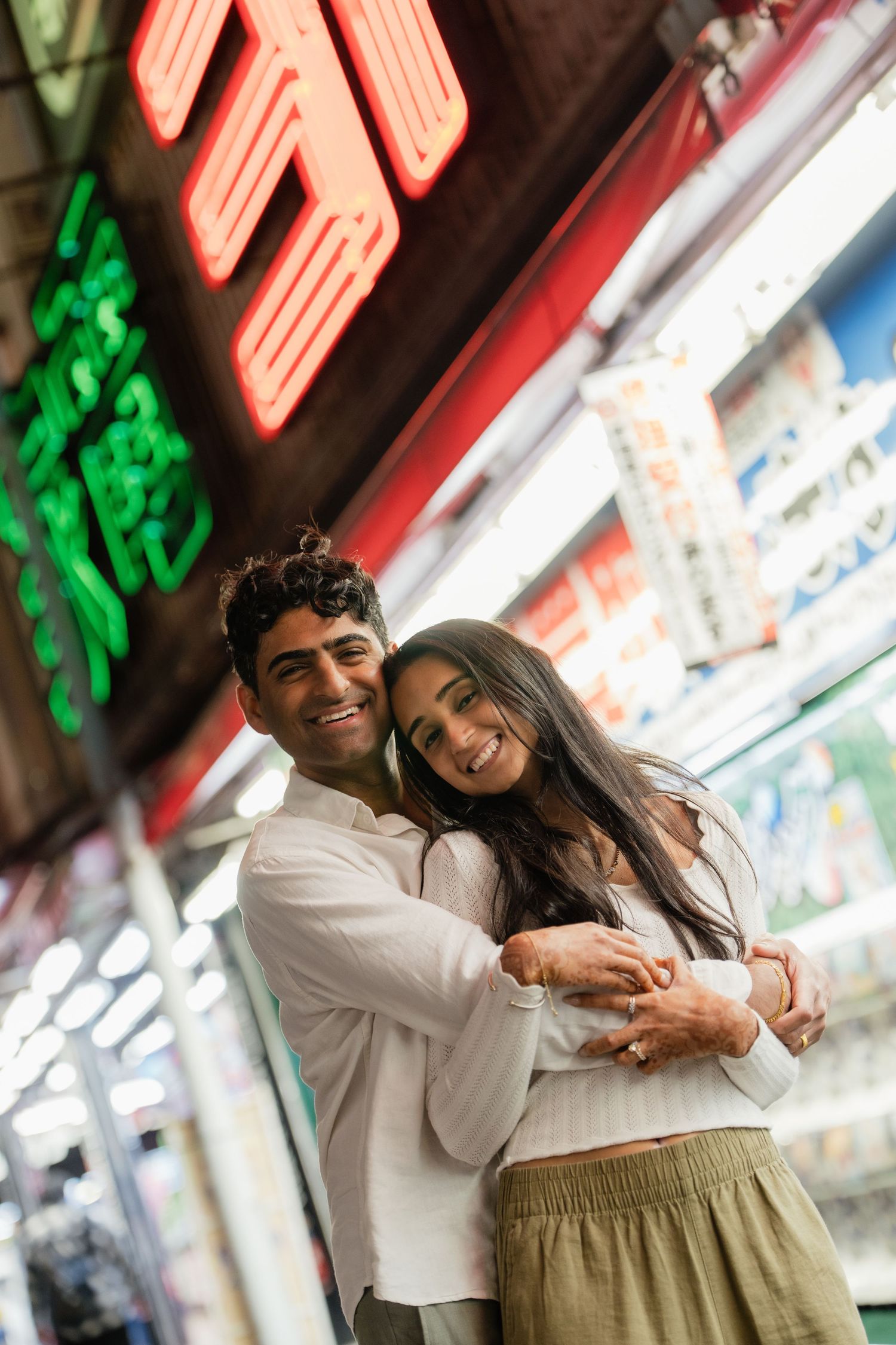 Happy couple embracing and smiling in front of colorful neon signs at a vibrant night market.