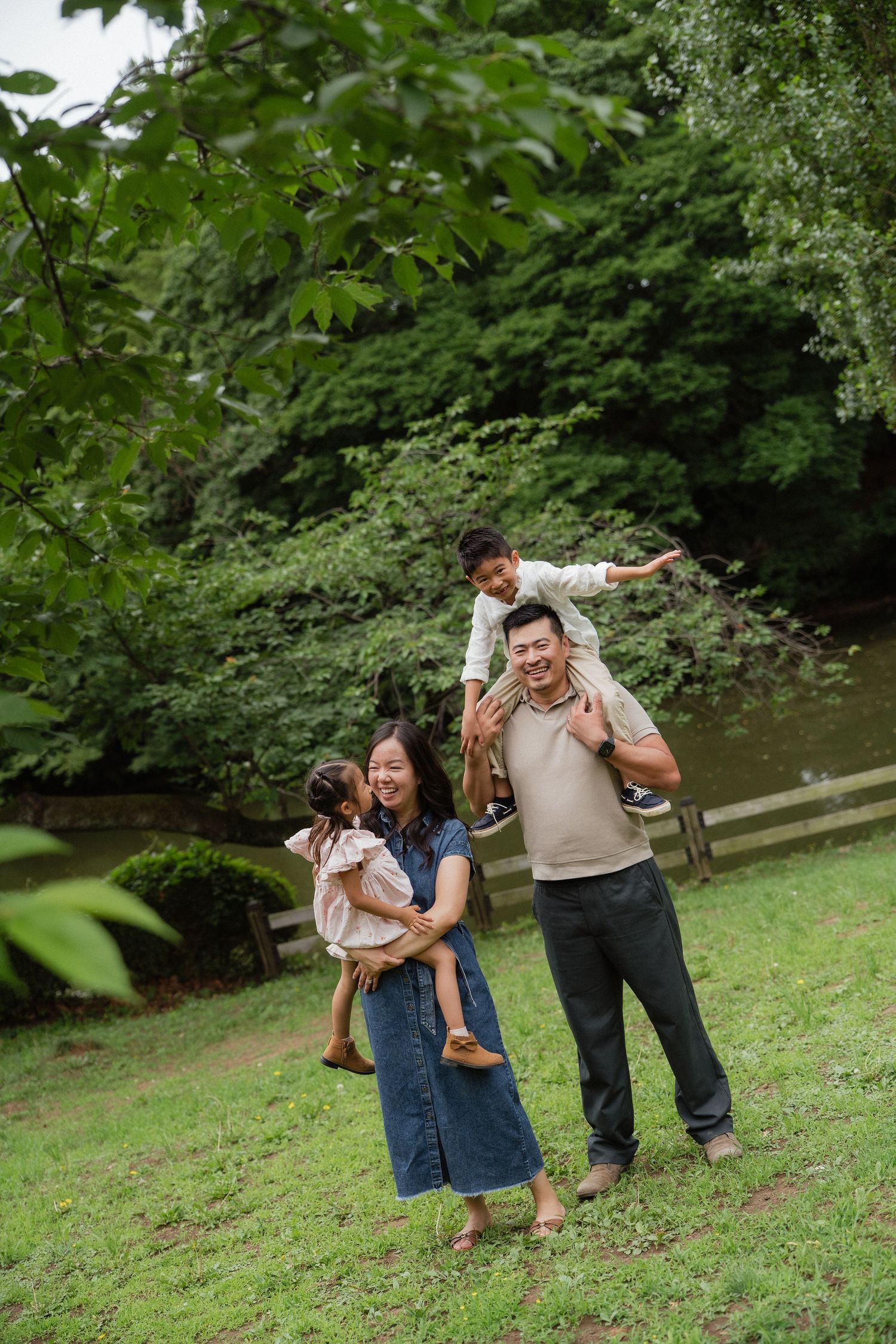 Happy Asian family enjoying outdoor time in a lush green park, parents carrying children on shoulders and arms.