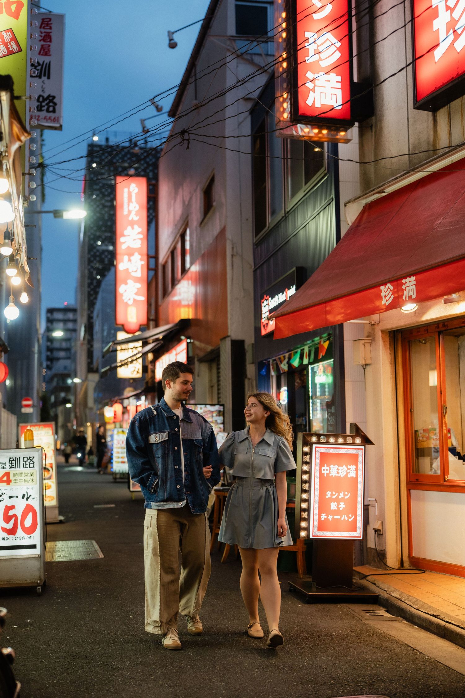 Couple walking hand in hand through a vibrant Japanese street at night, surrounded by glowing neon signs.