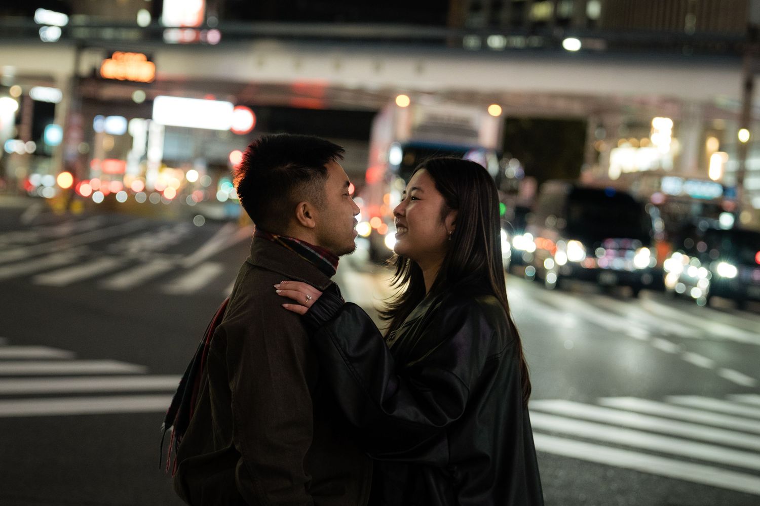 Couple sharing a romantic moment on a city street at night with blurred lights in the background.