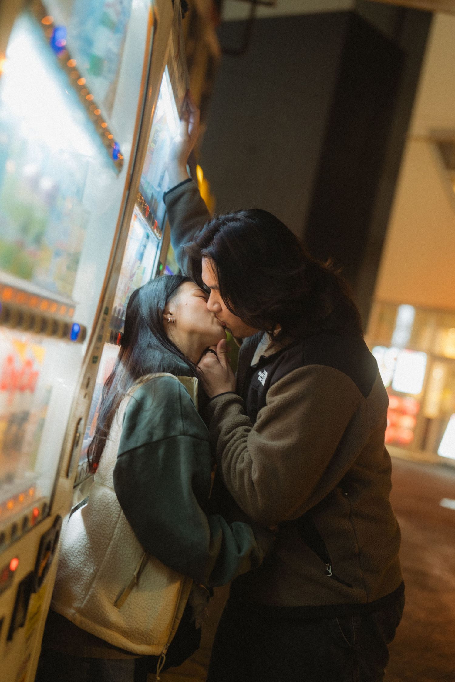 Couple sharing a romantic kiss beside a glowing vending machine at night in Japan.