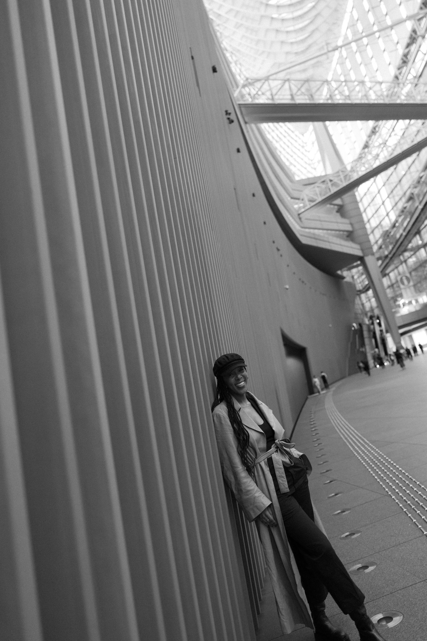 Black and white photo of a woman leaning against a curved wall in a modern building with a glass ceiling.