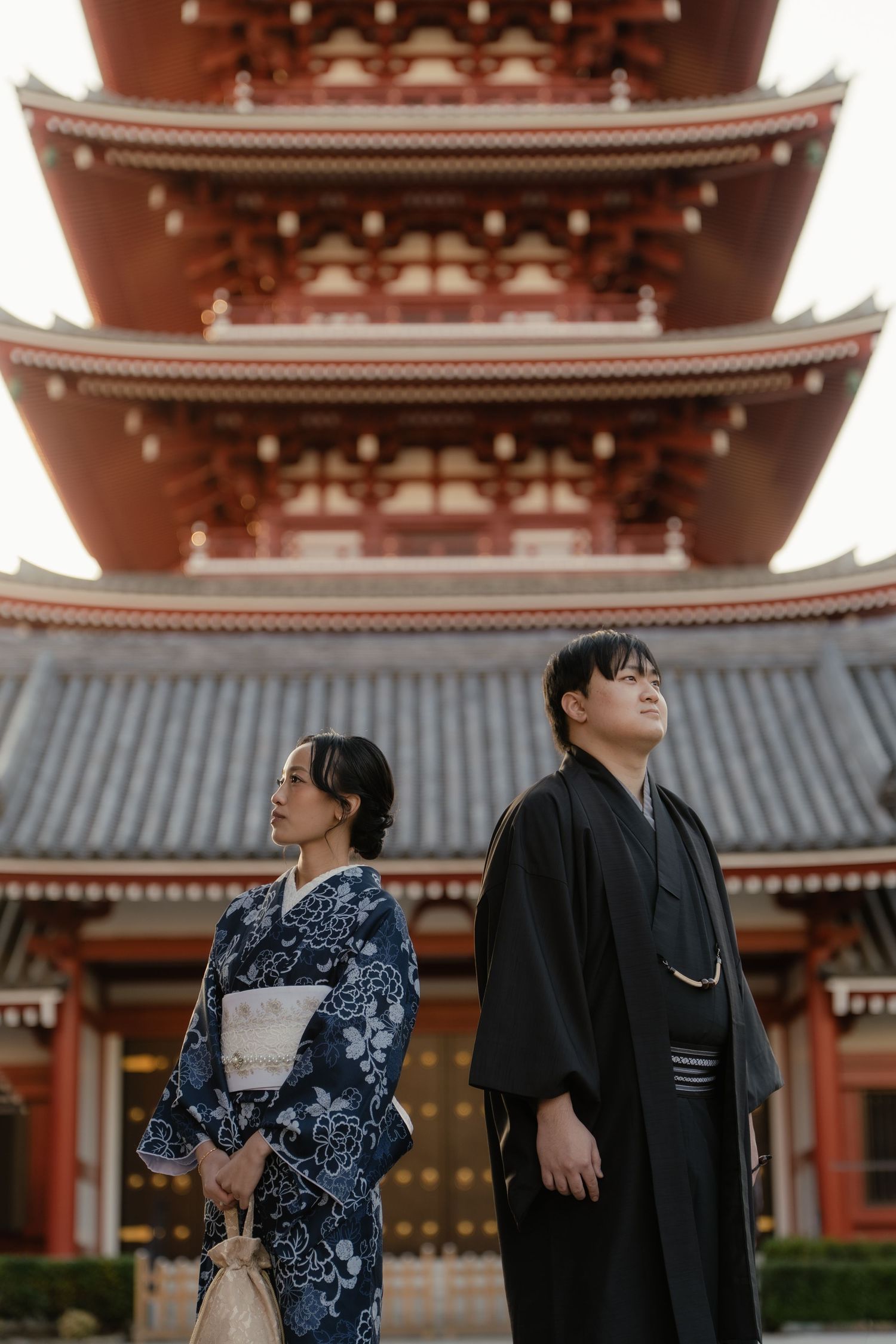 Couple in traditional Japanese kimono standing before a red multi-tiered pagoda at Senso-ji Temple, Tokyo.