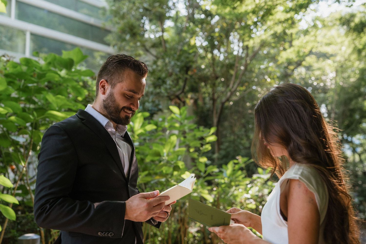 Bride and groom exchanging handwritten vows outdoors surrounded by lush green foliage during intimate wedding ceremony.
