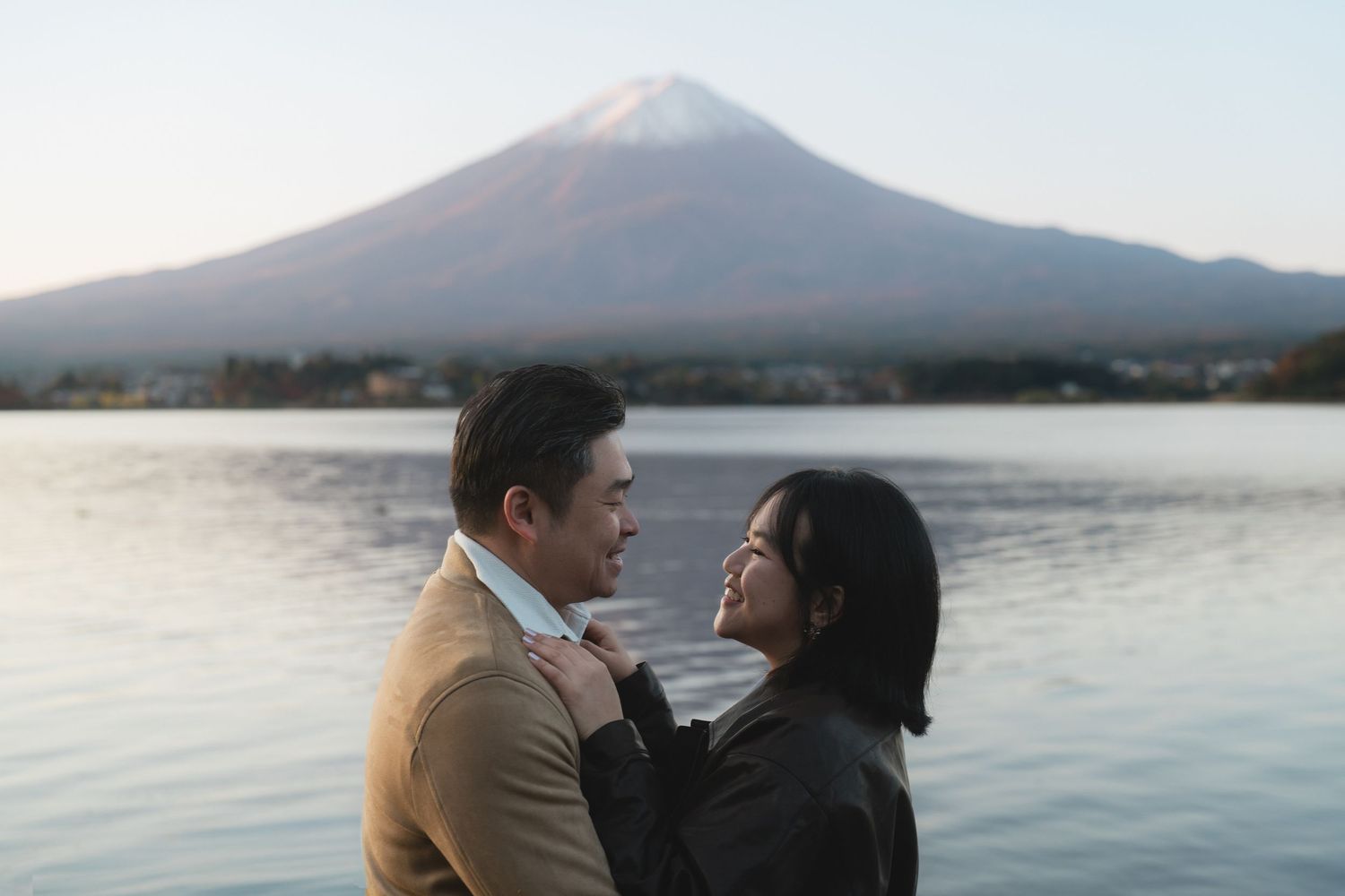 Couple sharing a romantic moment by a serene lake with iconic Mount Fuji in the background at sunset.